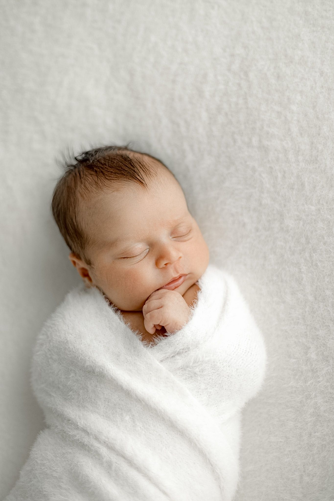 Peaceful newborn baby swaddled in white wrap sleeping on soft white blanket in professional newborn photography.
