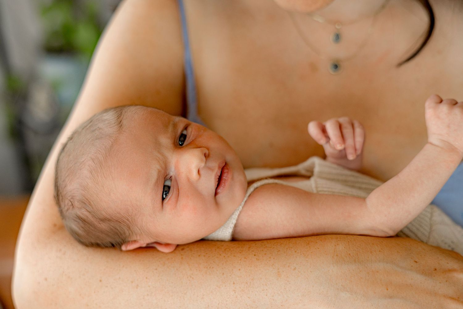 Newborn baby resting on mother's arm, looking up with alert eyes in a tender, intimate moment.