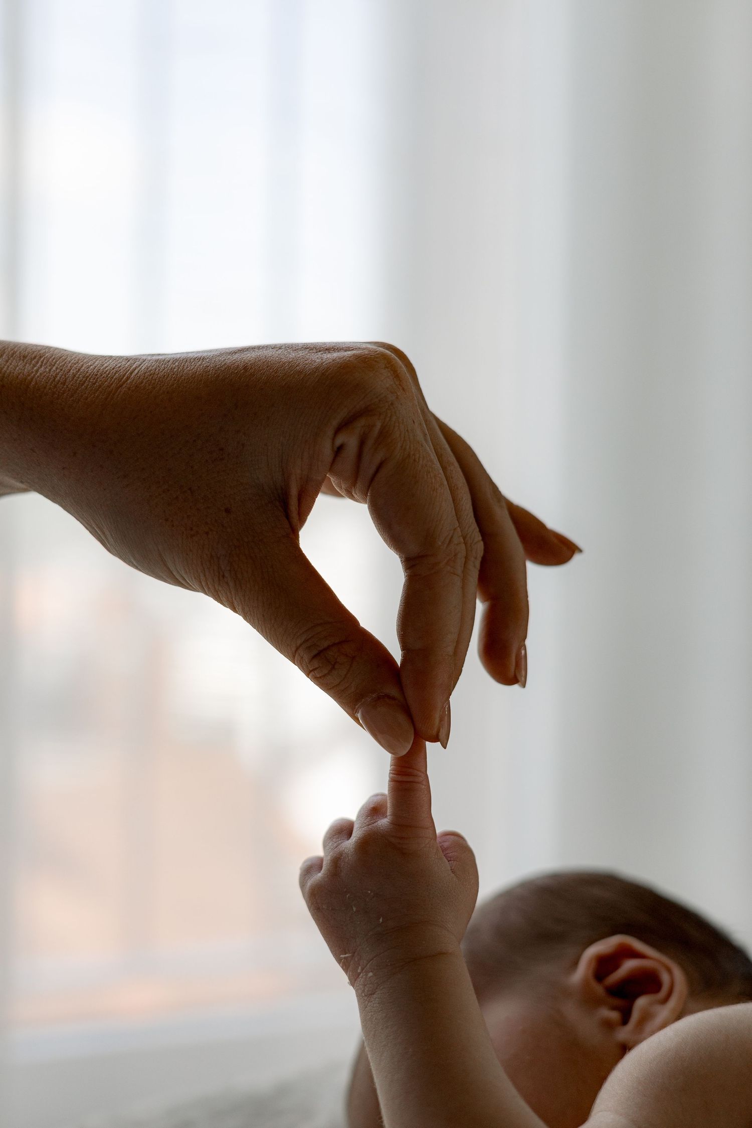 A mother's hand gently holds her newborn baby's tiny finger in a tender moment of connection.