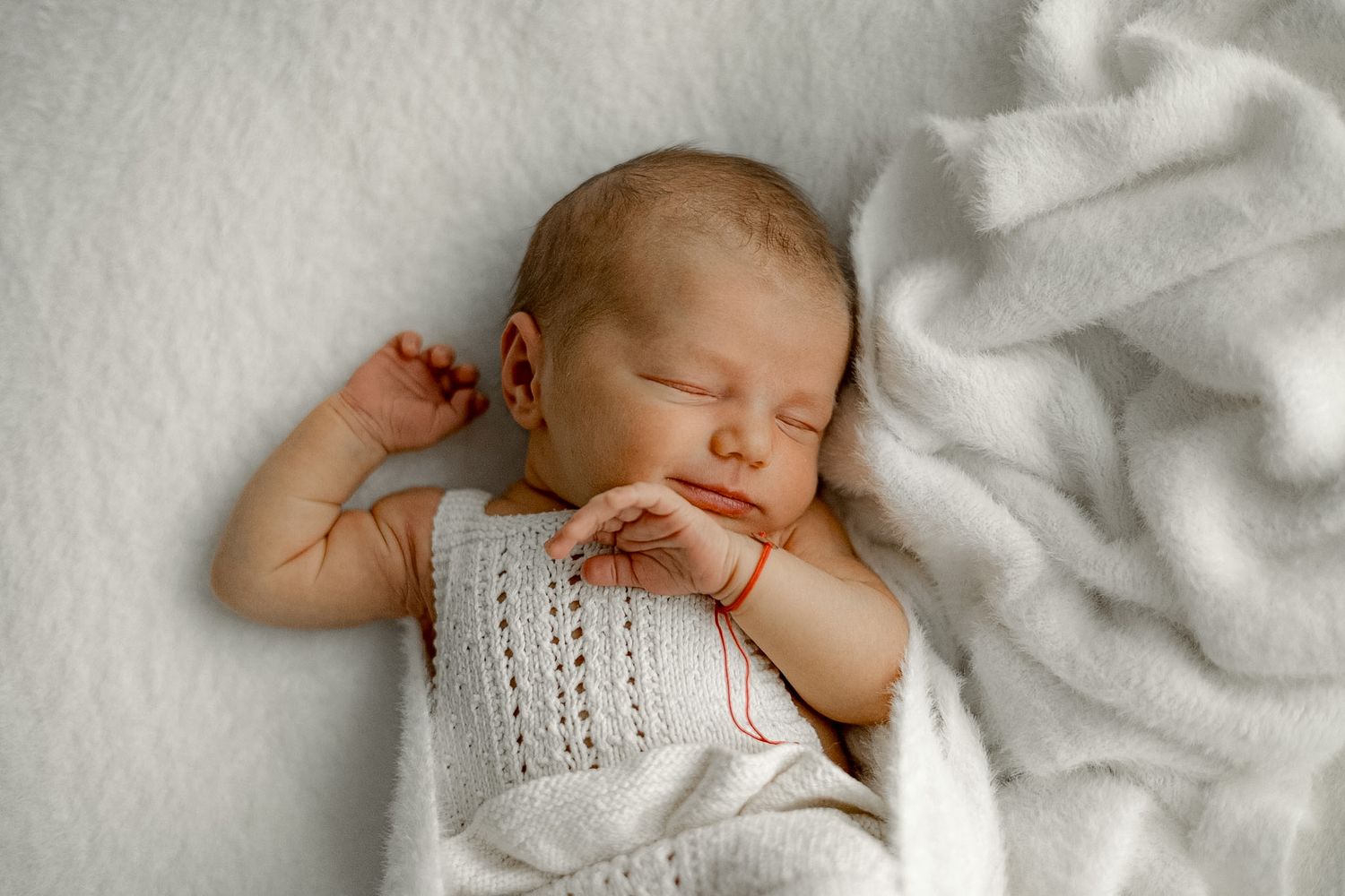 Peaceful newborn baby sleeping on white blanket wearing knit outfit, perfect newborn photography portrait.
