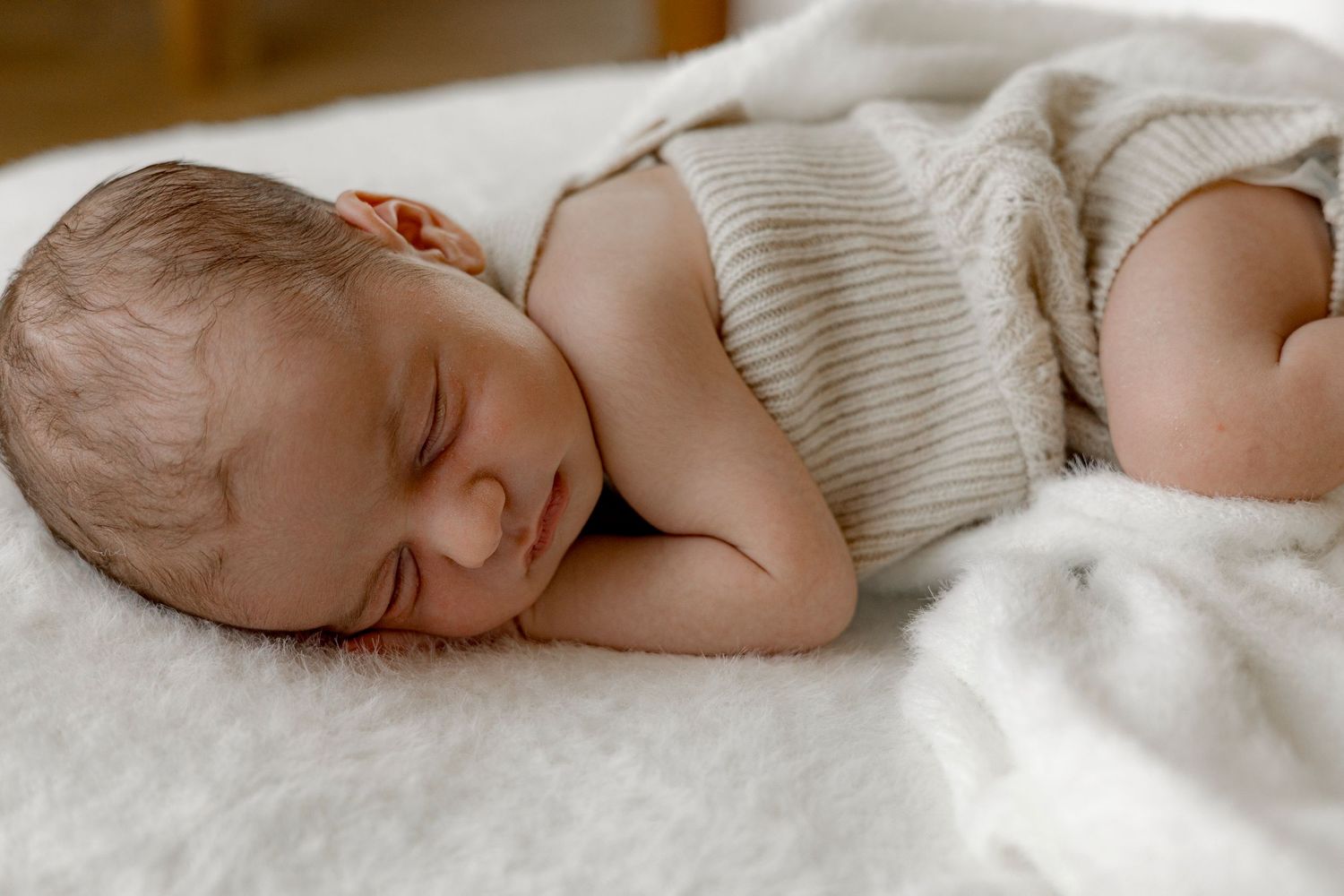 Newborn baby sleeping peacefully on a white fluffy blanket wearing a striped onesie.