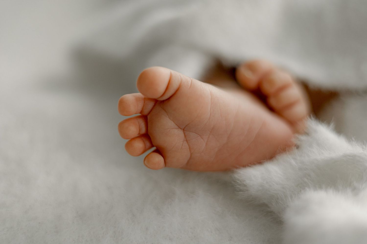 Close-up of tiny newborn baby feet resting on a soft white blanket, showcasing delicate toes and smooth skin.