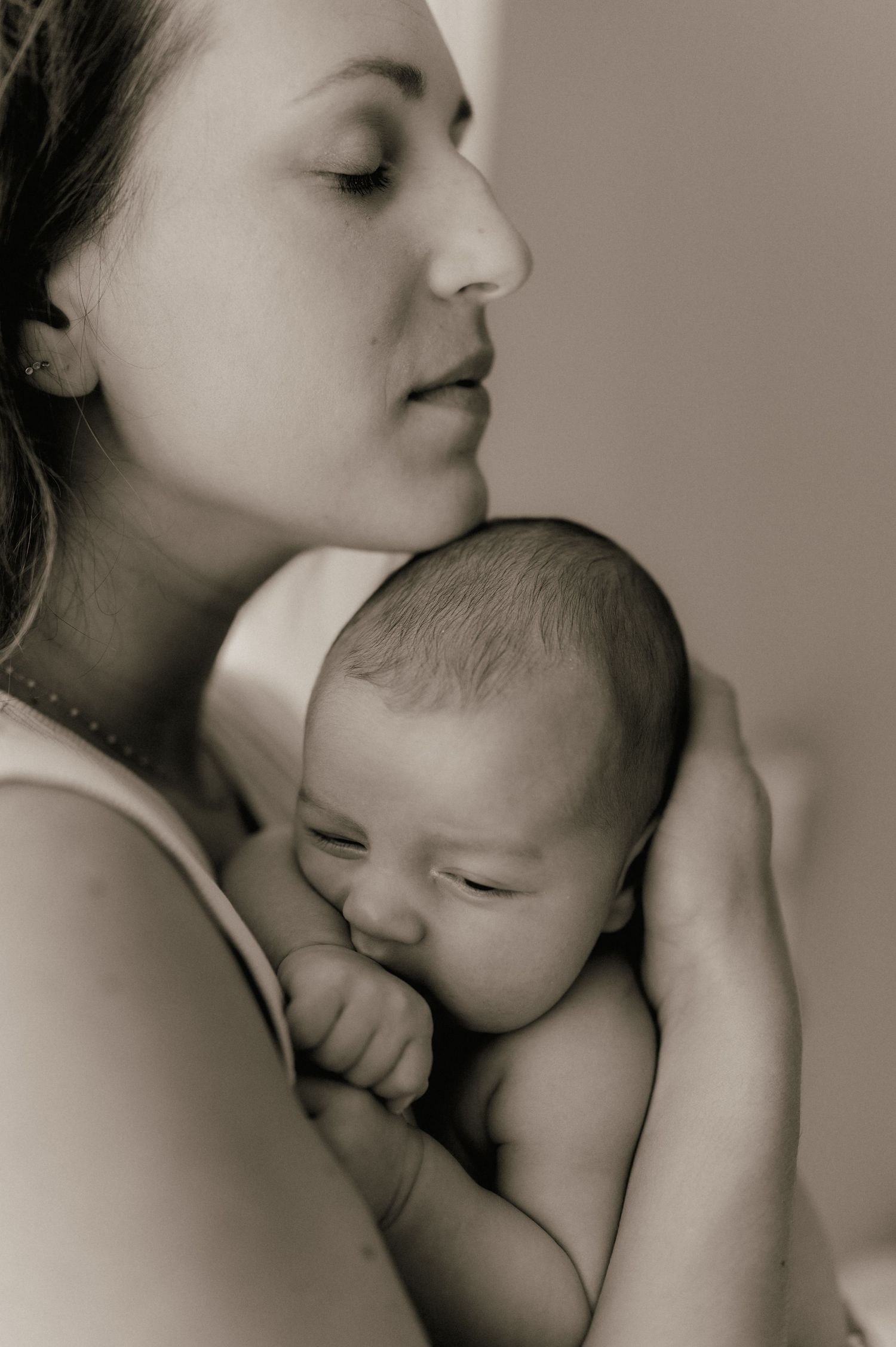 Serene black and white portrait of a mother gently holding her sleeping newborn baby close.