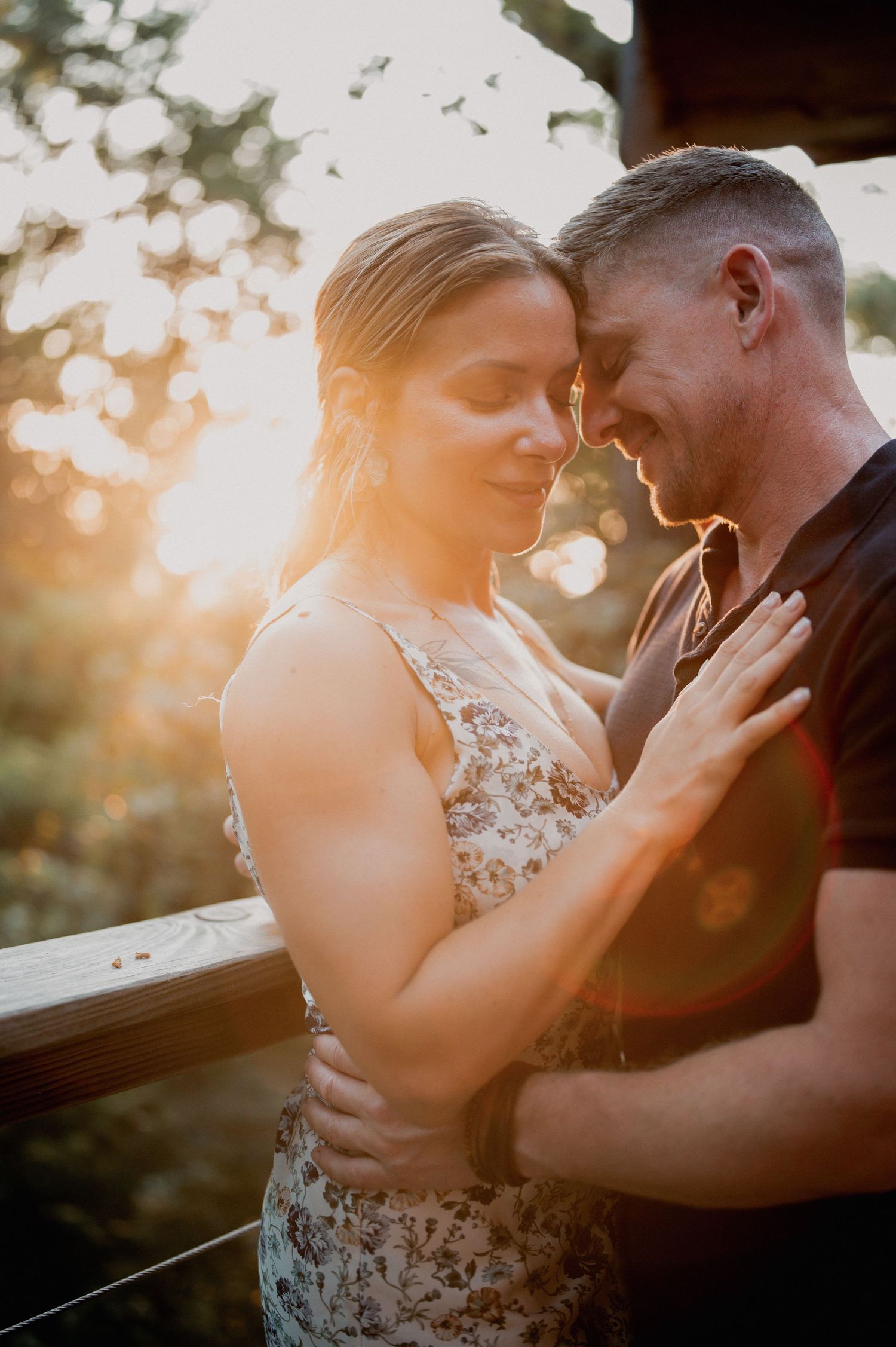 Couple embracing tenderly at golden sunset on wooden deck outdoors.