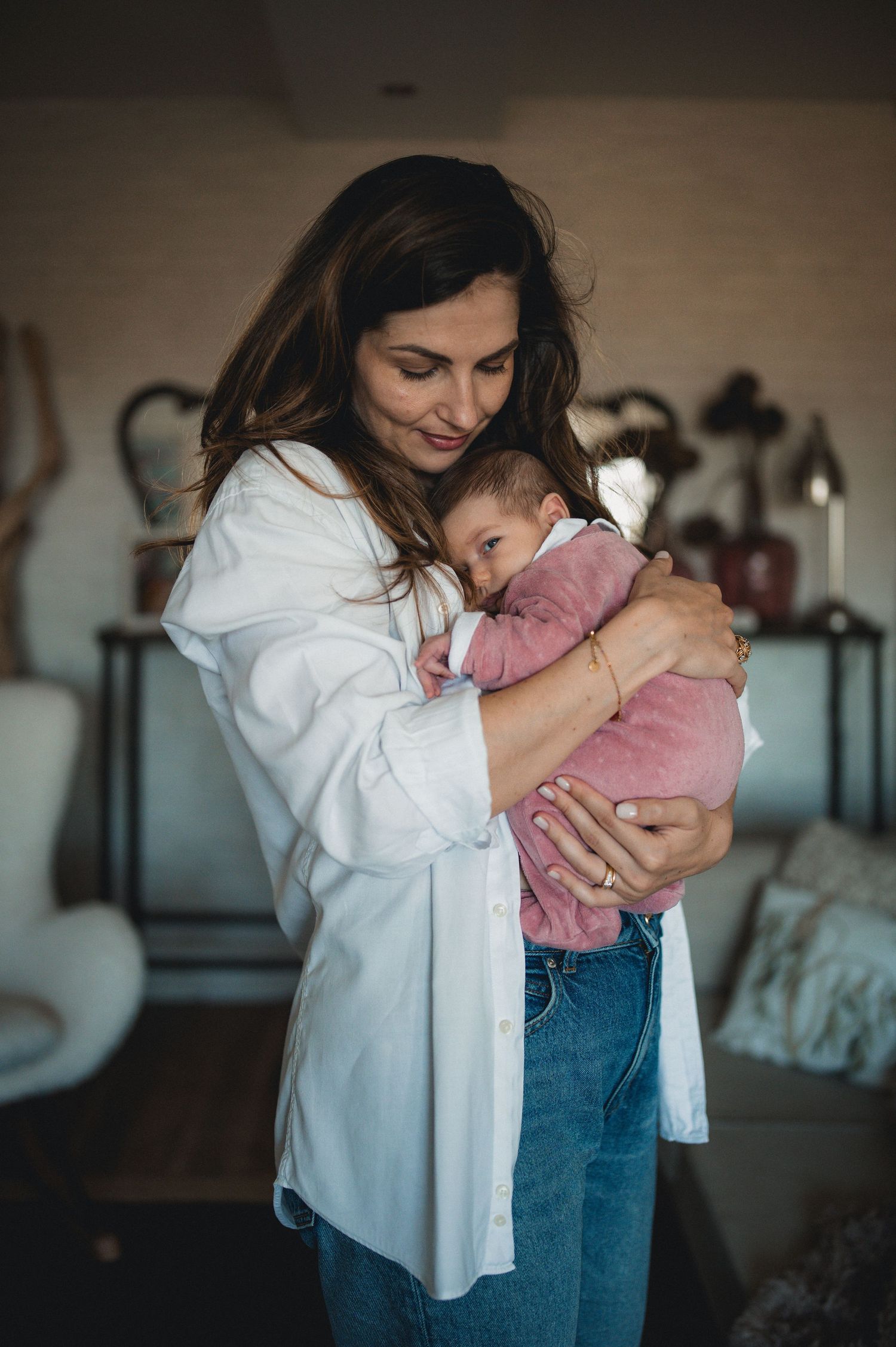 Loving mother in white shirt tenderly cradling her newborn baby dressed in pink in a cozy home setting.