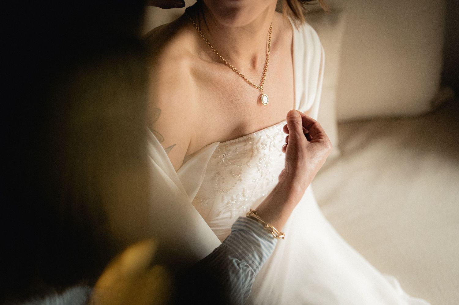 Close-up of bride in strapless lace wedding gown fastening a delicate pearl necklace.