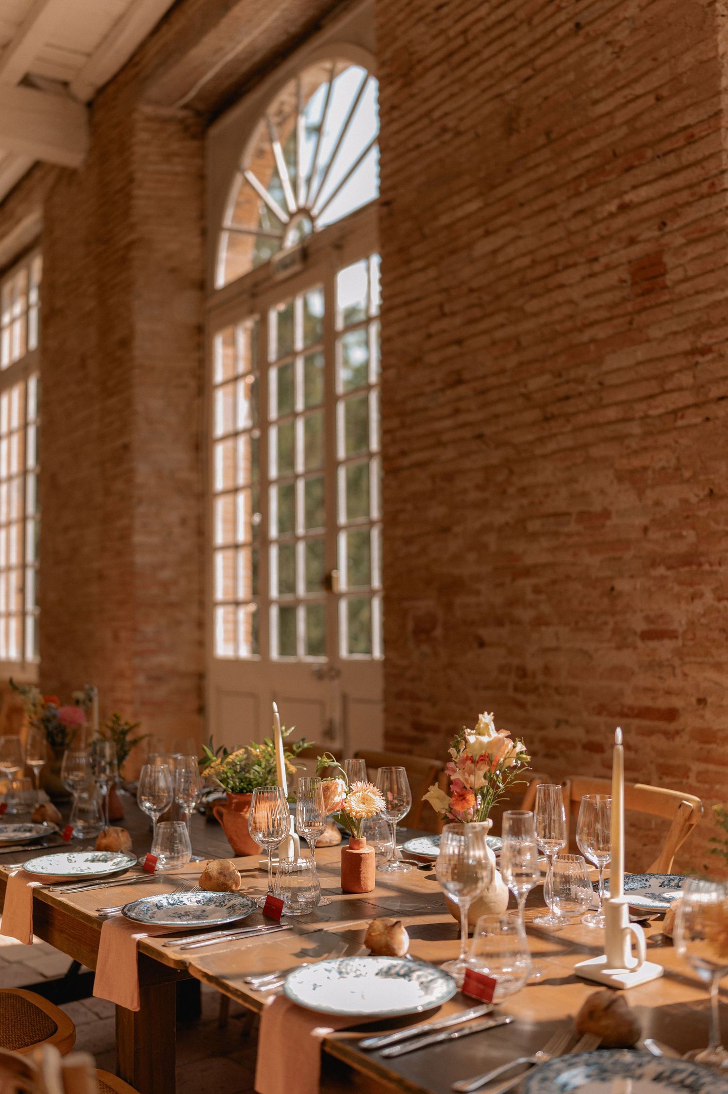 Elegant wedding reception table set in rustic brick venue with floral centerpieces.