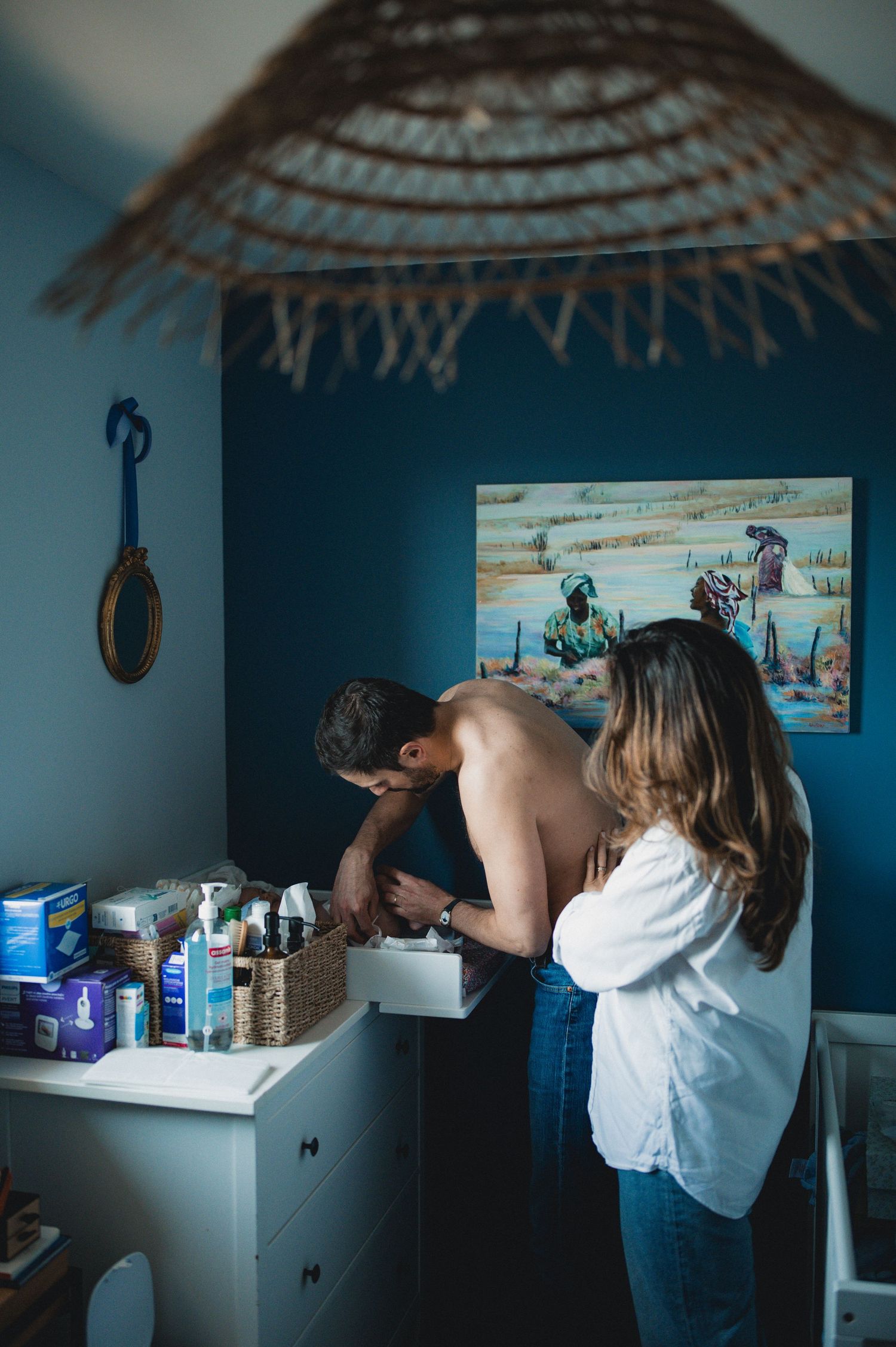 Shirtless father and mother preparing baby items at a changing table in a blue nursery.