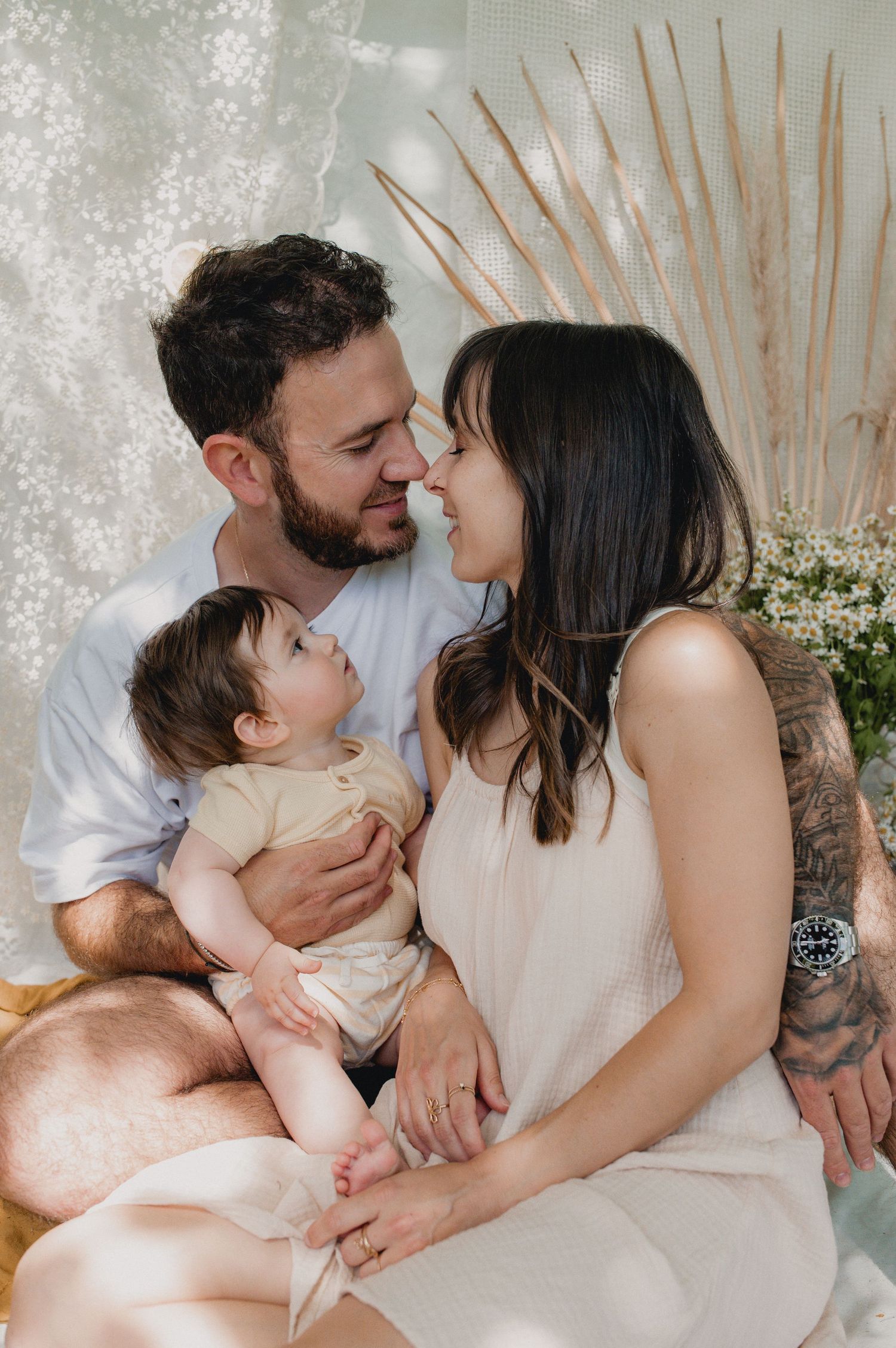 A young couple shares a nose kiss while holding their baby during a soft studio family session.