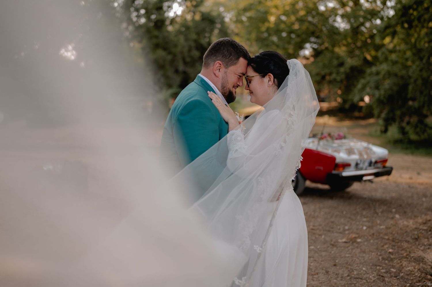 Bride and groom embracing romantically with wedding veil flowing in wind.