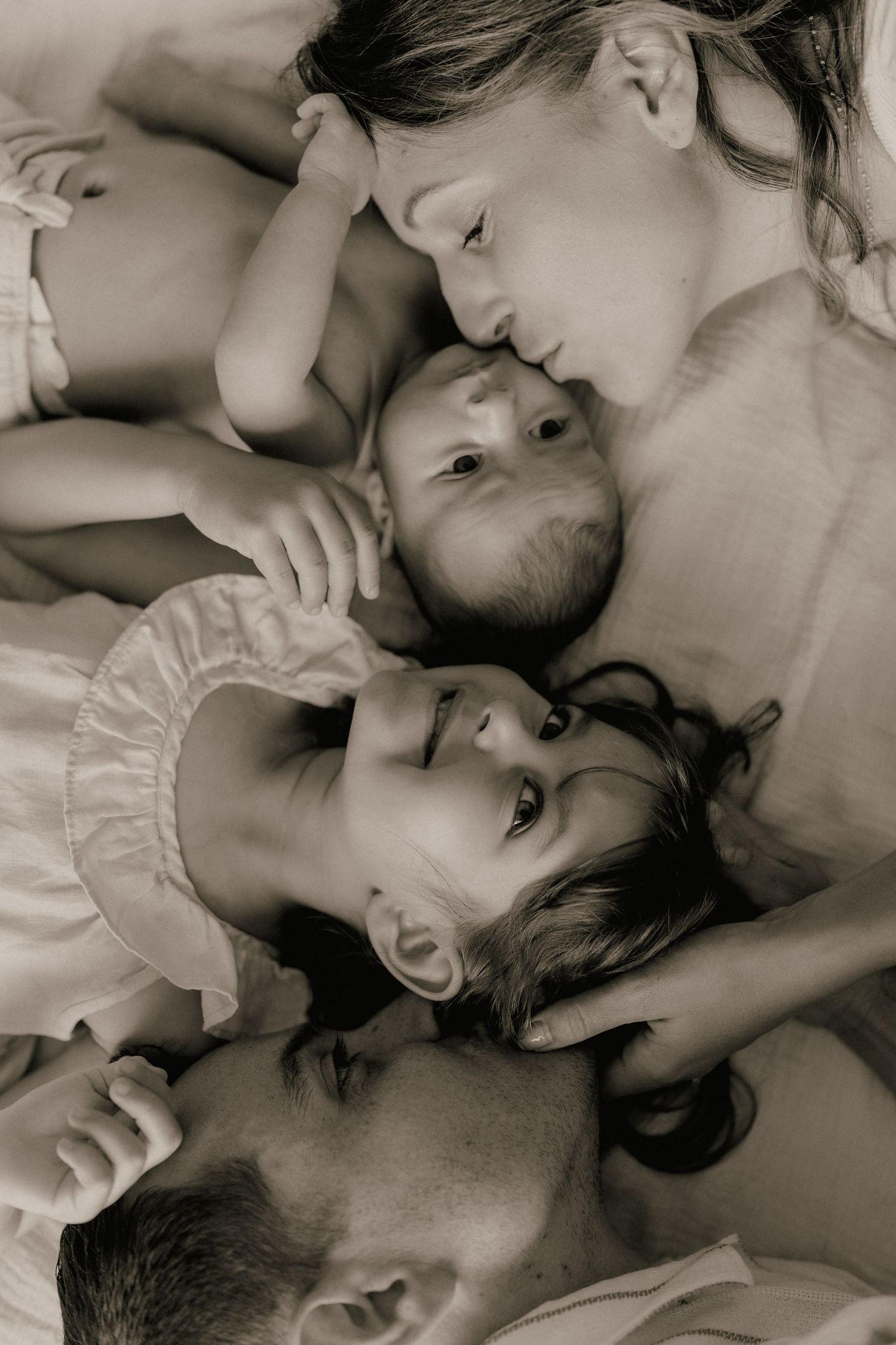 A black and white overhead portrait of parents and two young children lying together closely.