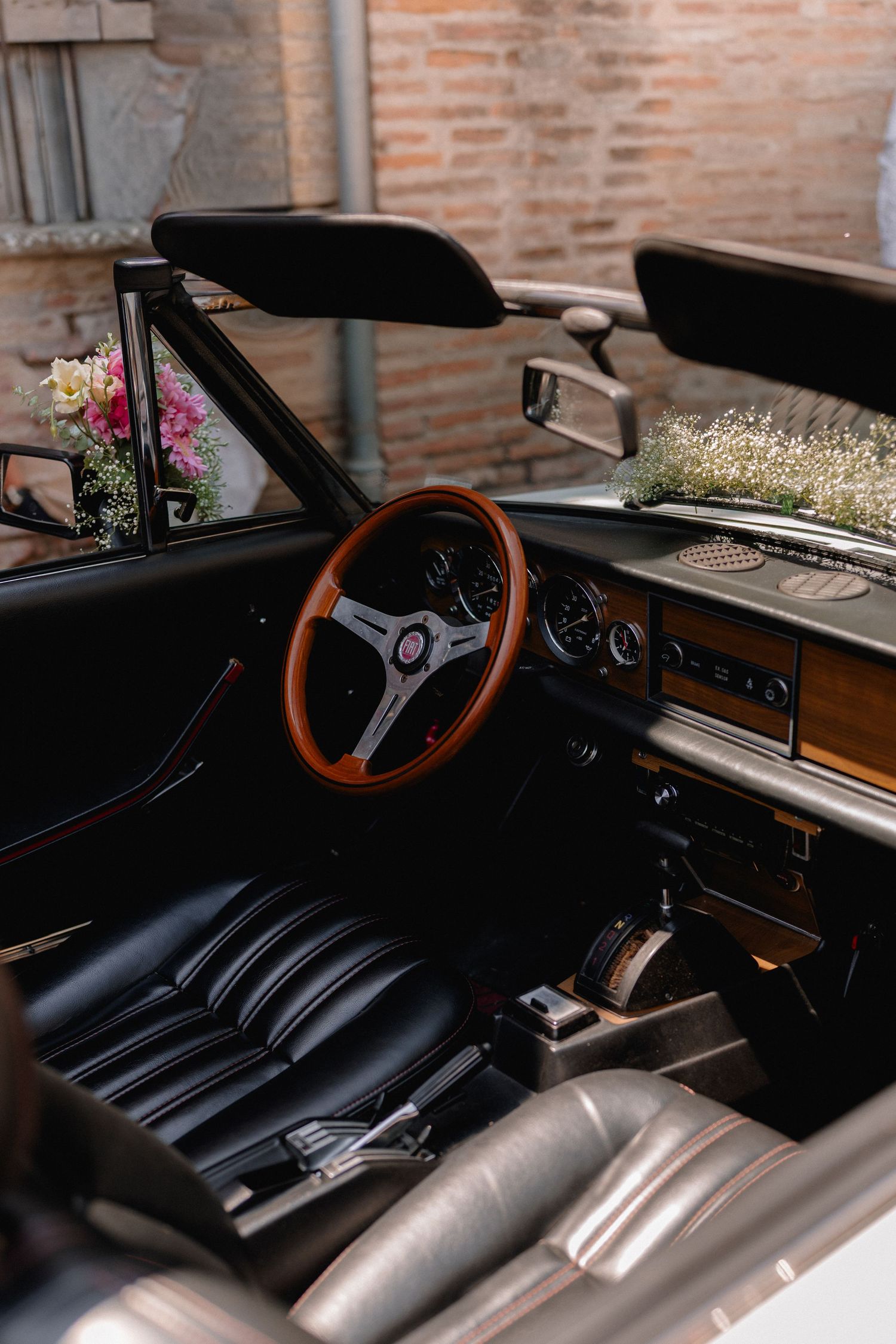 Classic vintage convertible car interior with wooden steering wheel and floral decorations.