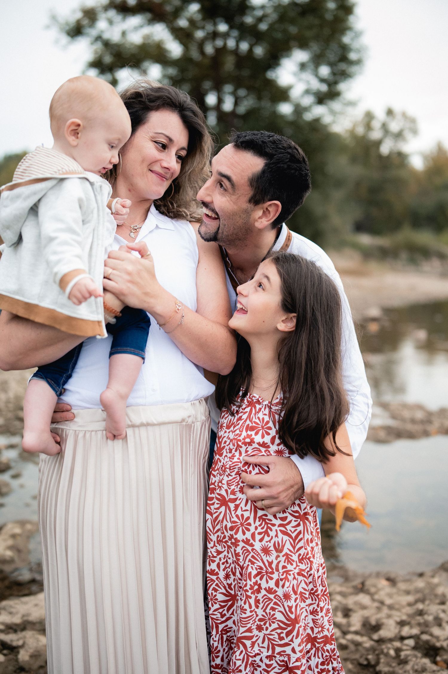 Loving family of four embracing near a river during a warm autumn outdoor photography session.