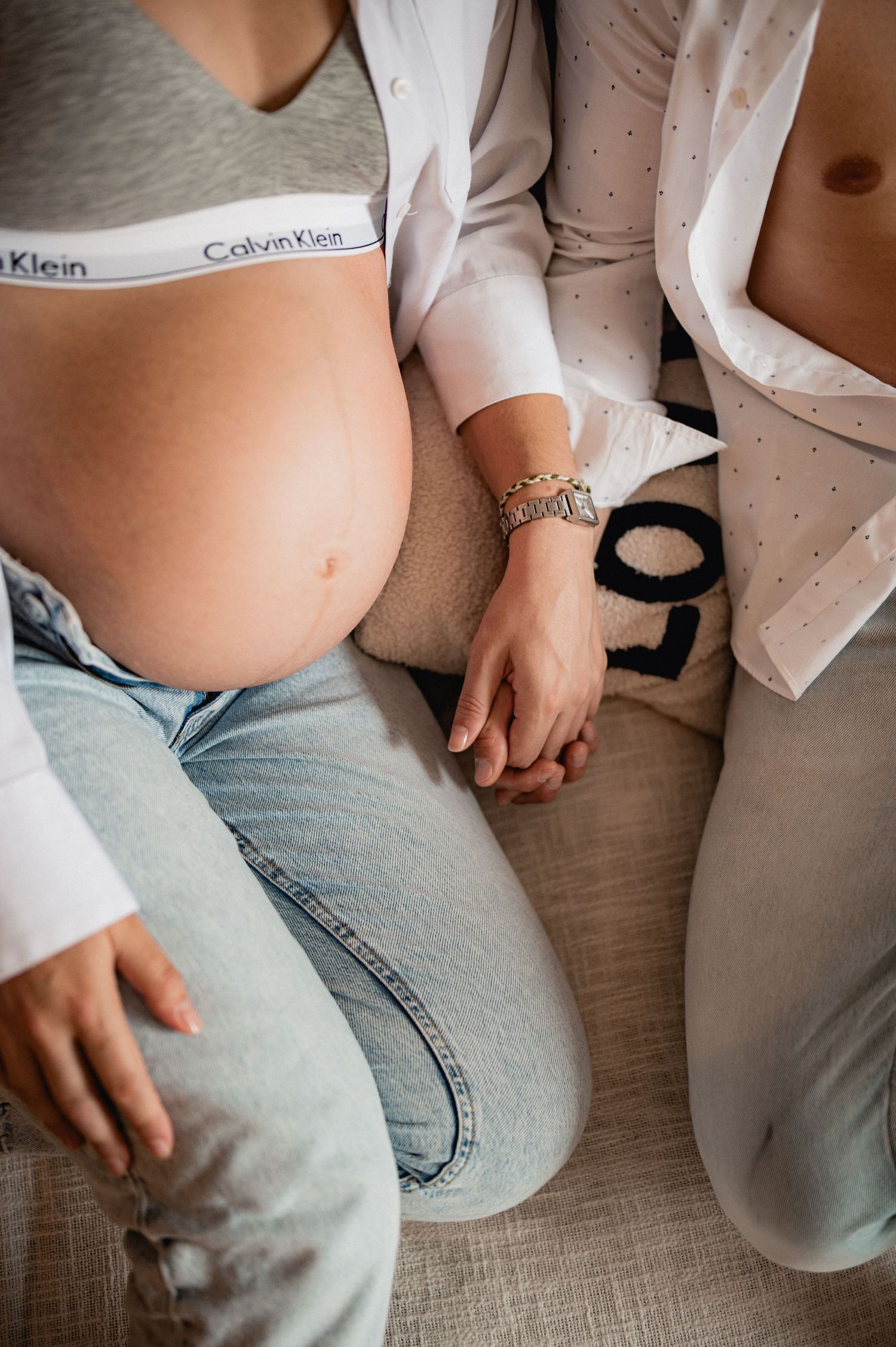 Close-up of pregnant woman in Calvin Klein underwear holding hands with partner during intimate maternity session.