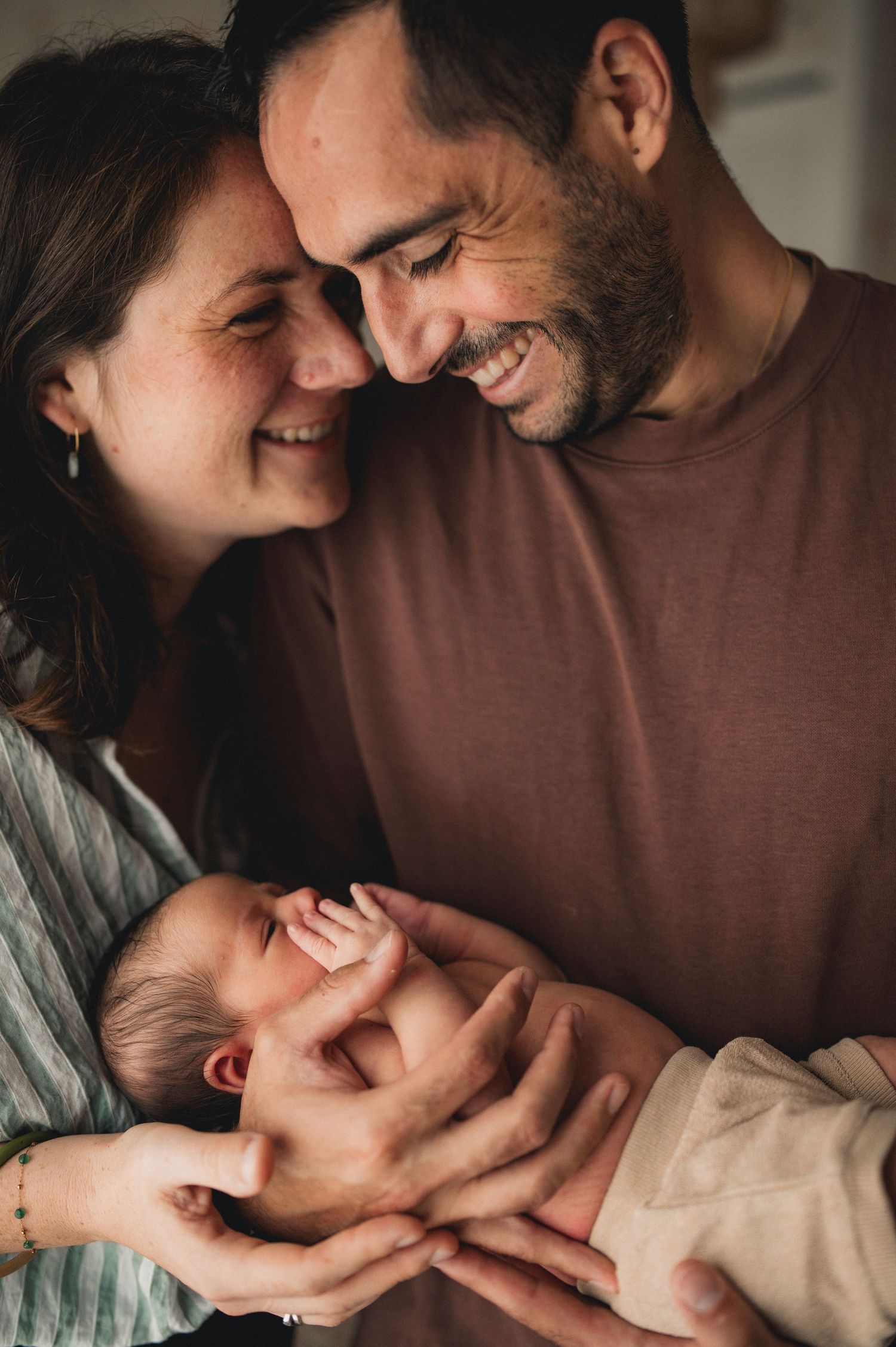 Smiling parents touching foreheads lovingly while holding their newborn baby.