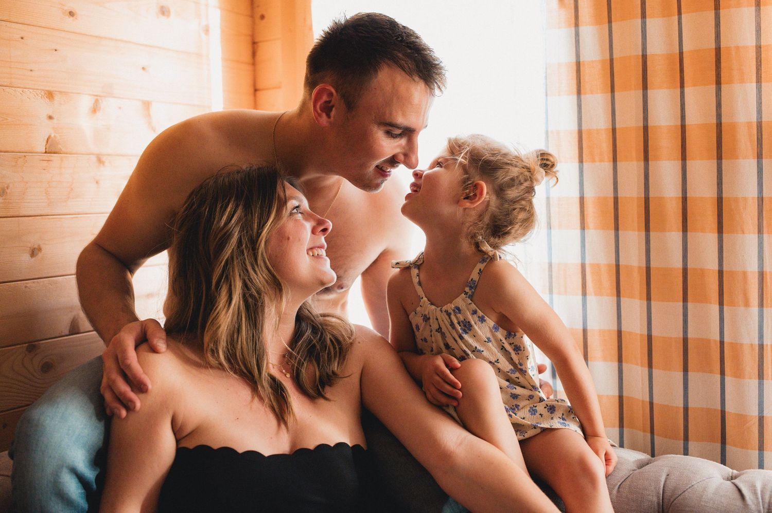 Loving family of three sharing a tender moment together in a cozy wooden cabin bedroom.