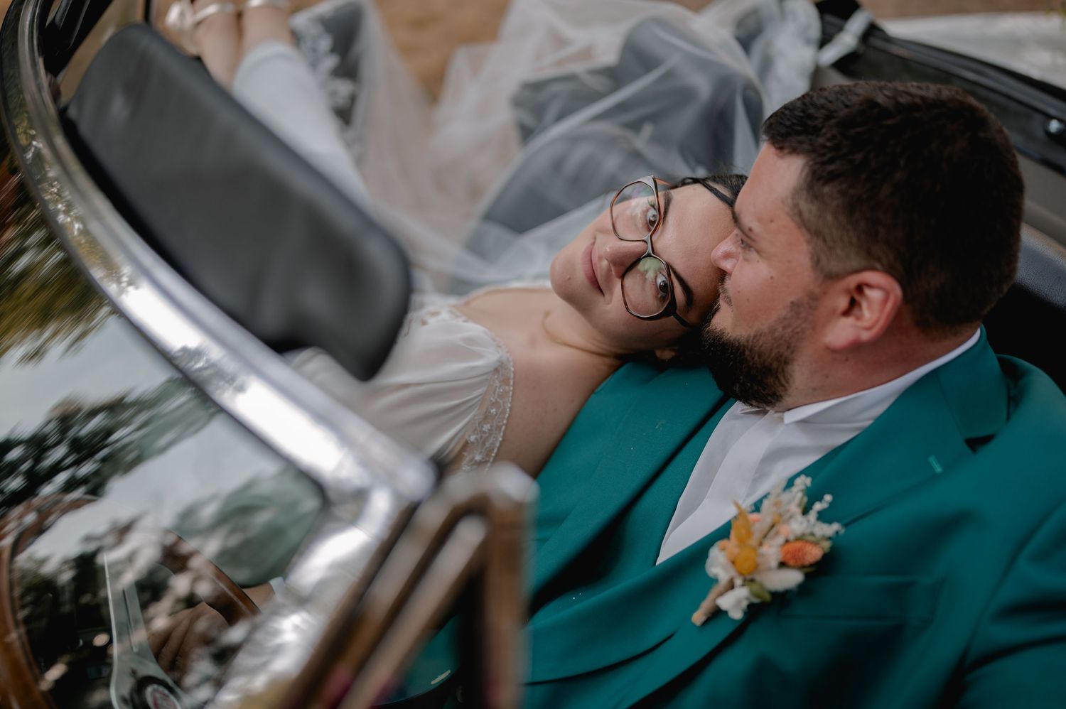 Bride and groom share romantic kiss in vintage convertible car on wedding day.