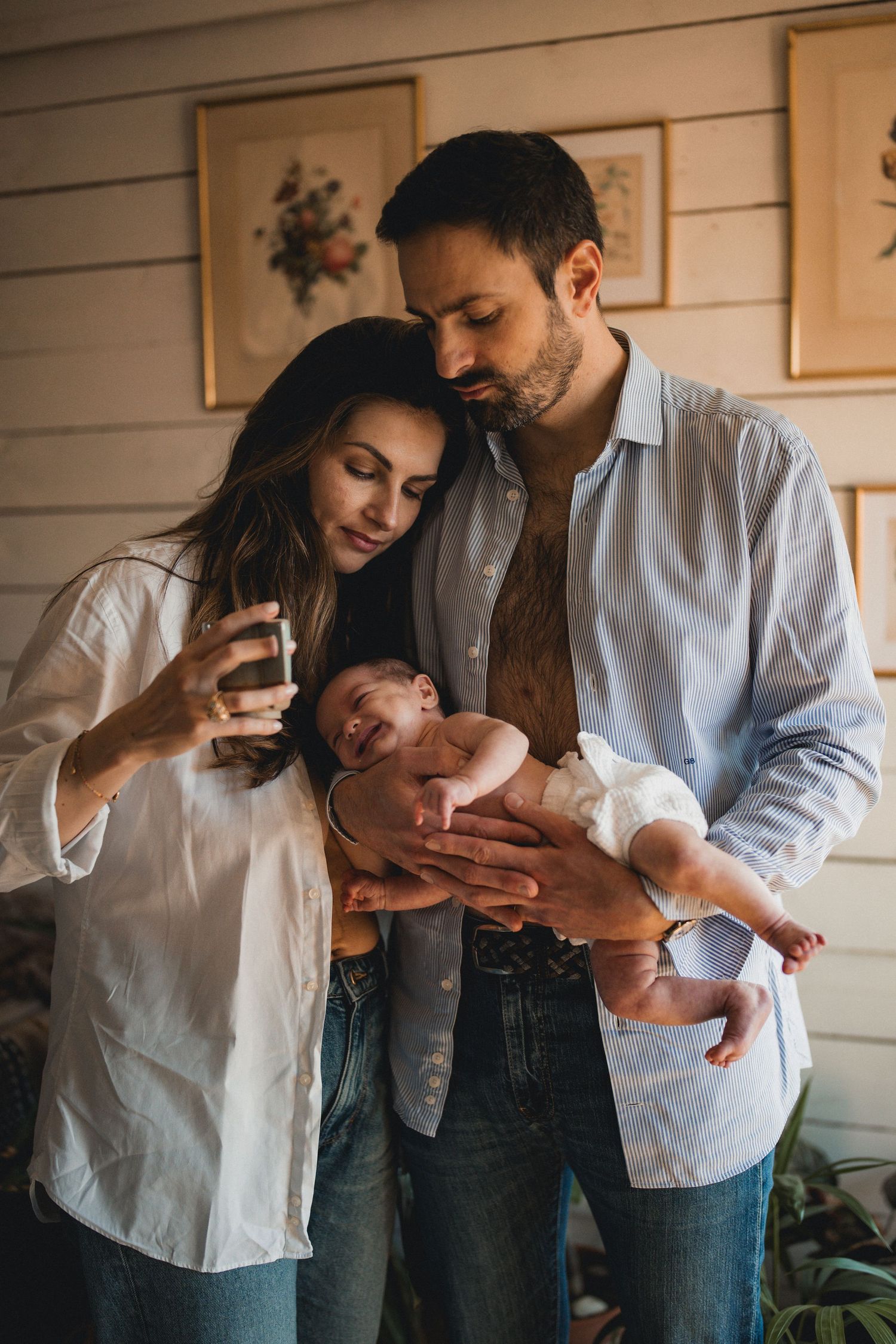 Happy couple standing together holding their newborn baby indoors at home.