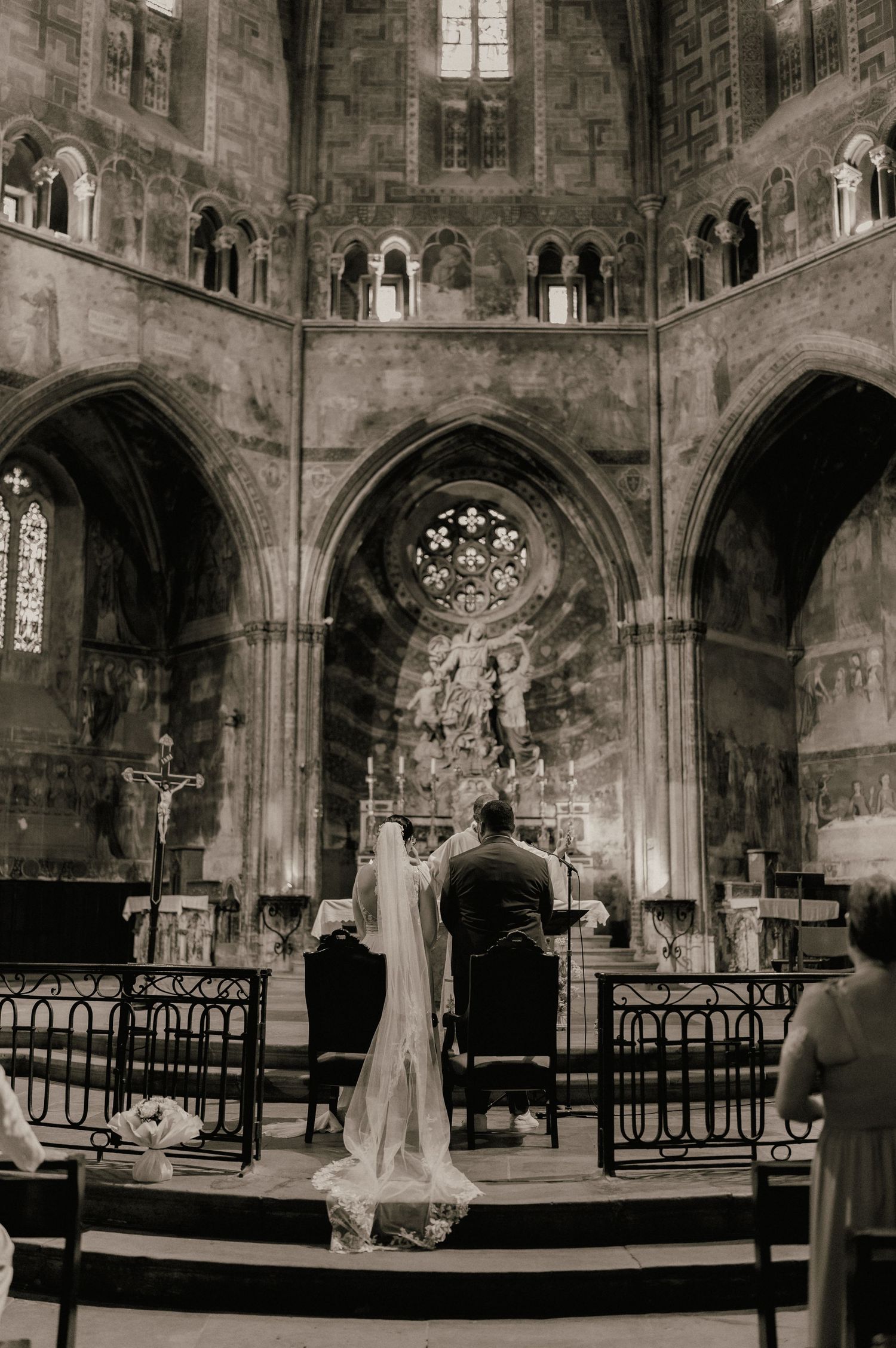 Black and white photo of a bride and groom kneeling at the altar of a grand historic cathedral during their wedding ceremony.