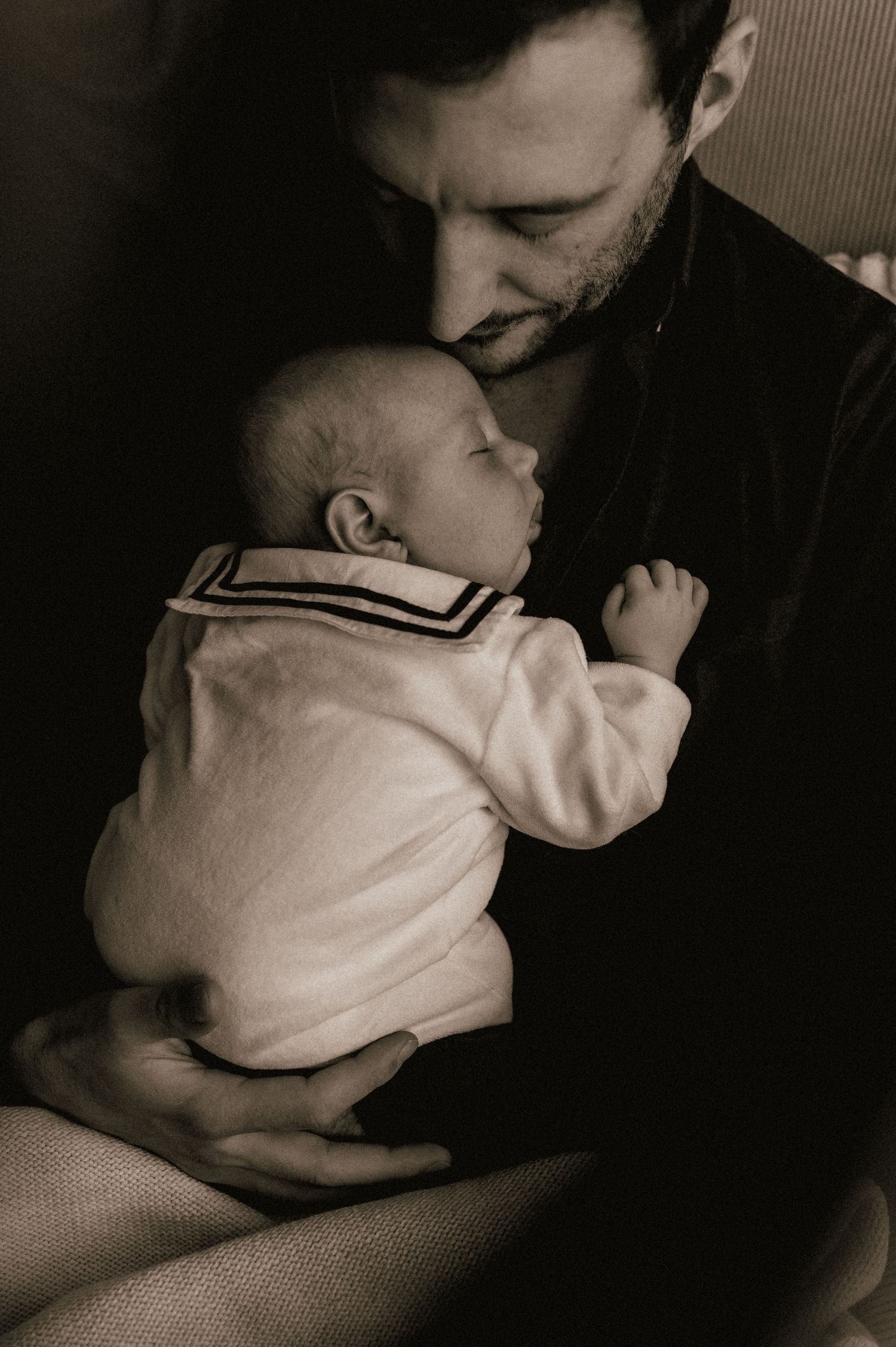Tender black and white portrait of a father gently kissing his sleeping newborn baby.