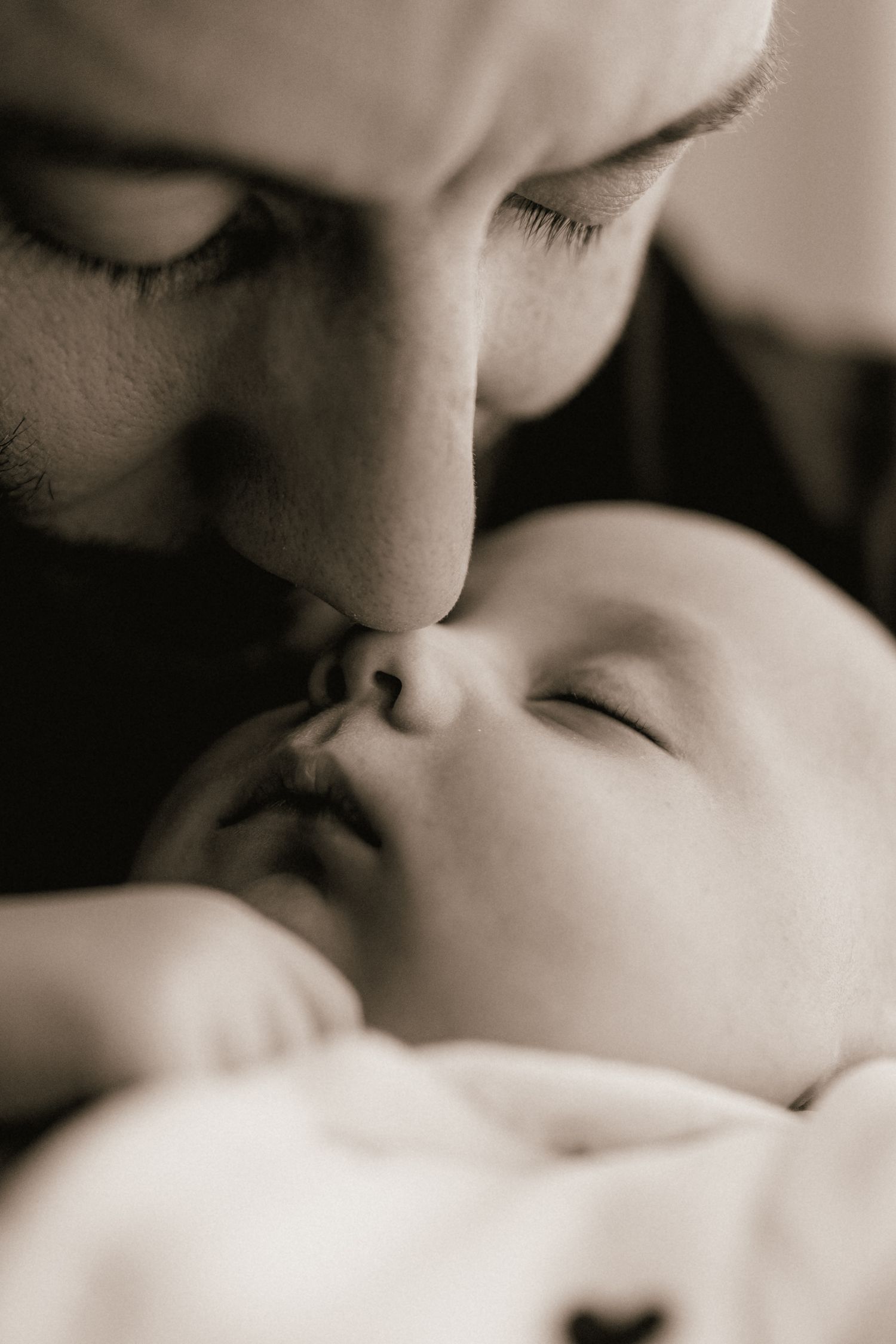 Black and white photo of parent kissing sleeping newborn baby softly.