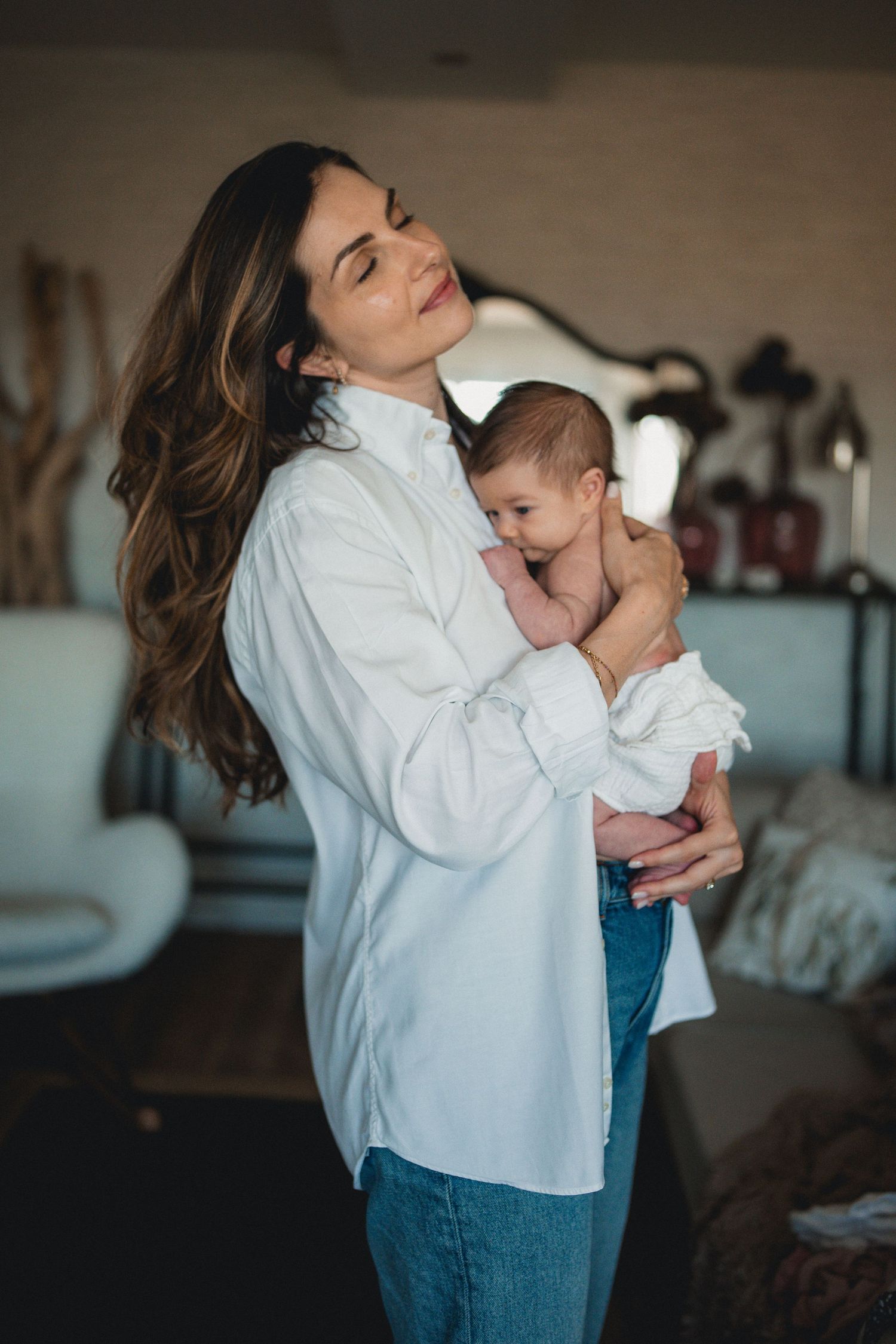 Beautiful mother with long hair holding her newborn baby in a cozy home setting.