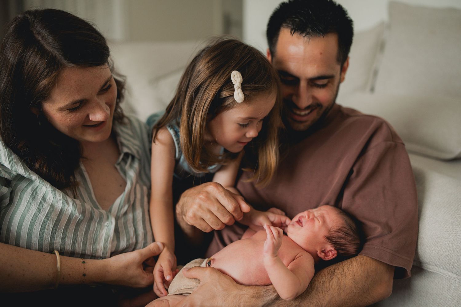 Happy family with mother, father, young daughter, and newborn baby bonding together at home.