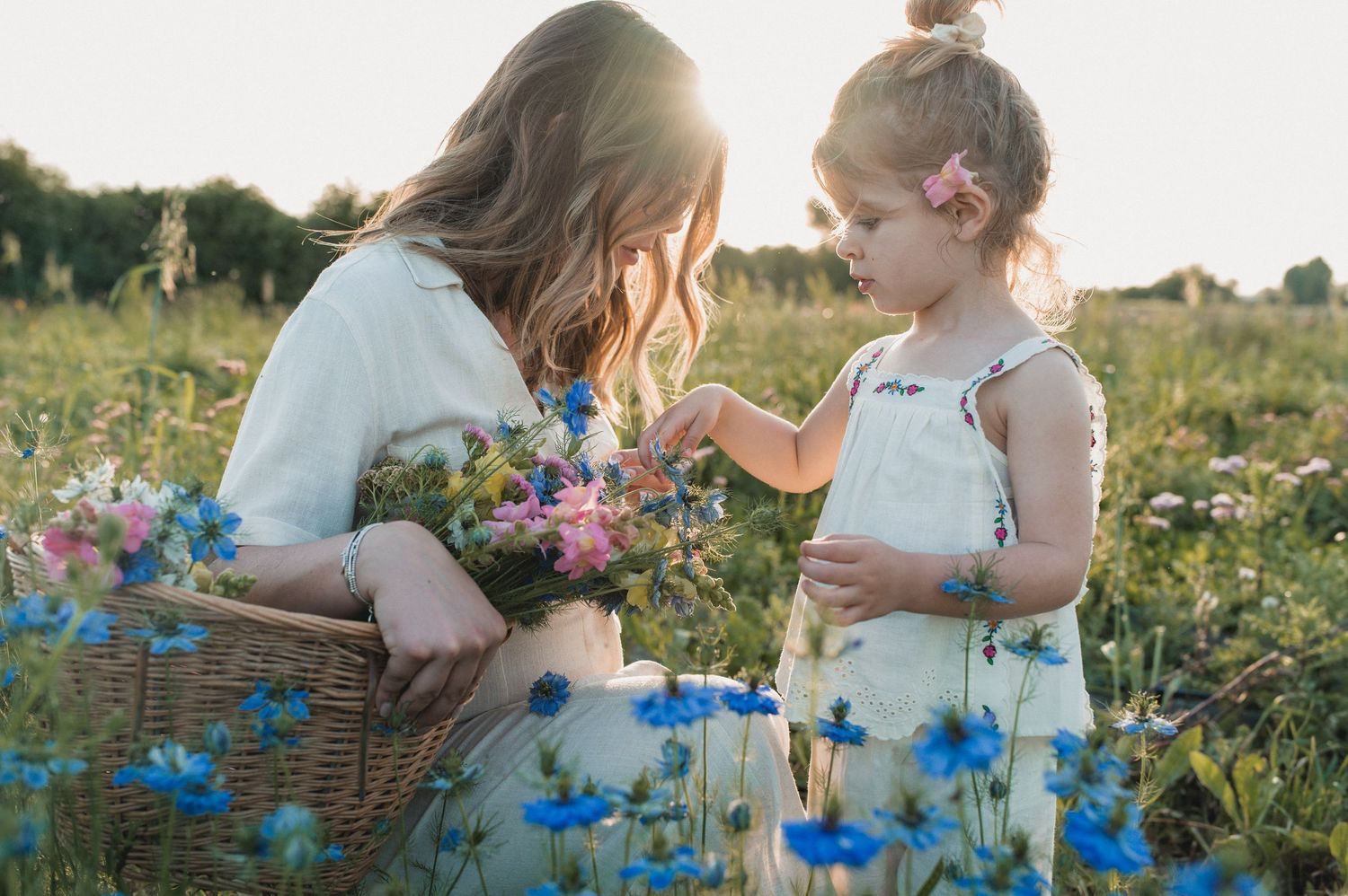 A mother and young daughter share a sweet moment picking wildflowers in a sunny meadow.