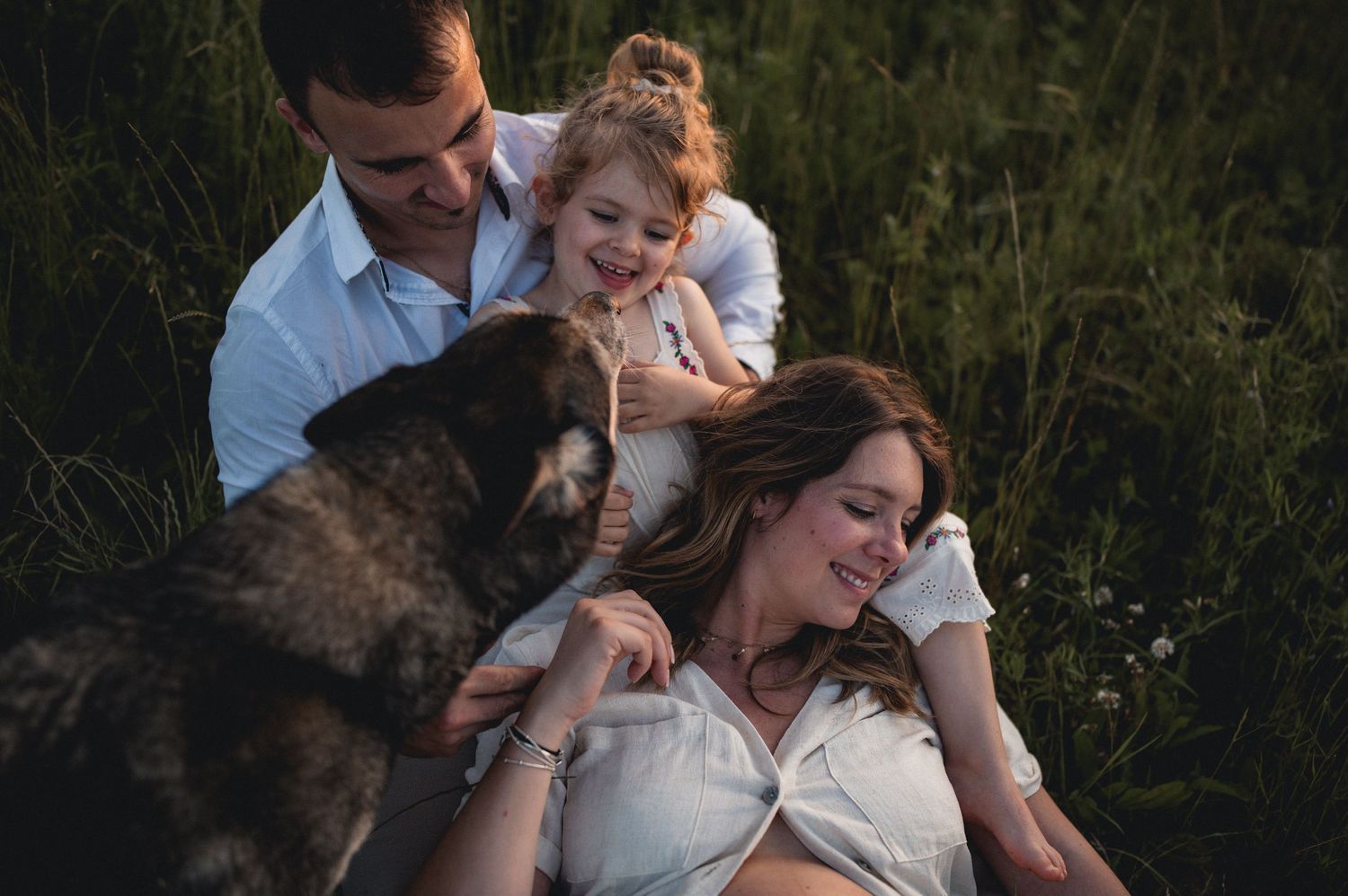 A happy family with a dog relaxes together in a lush green field at golden hour.