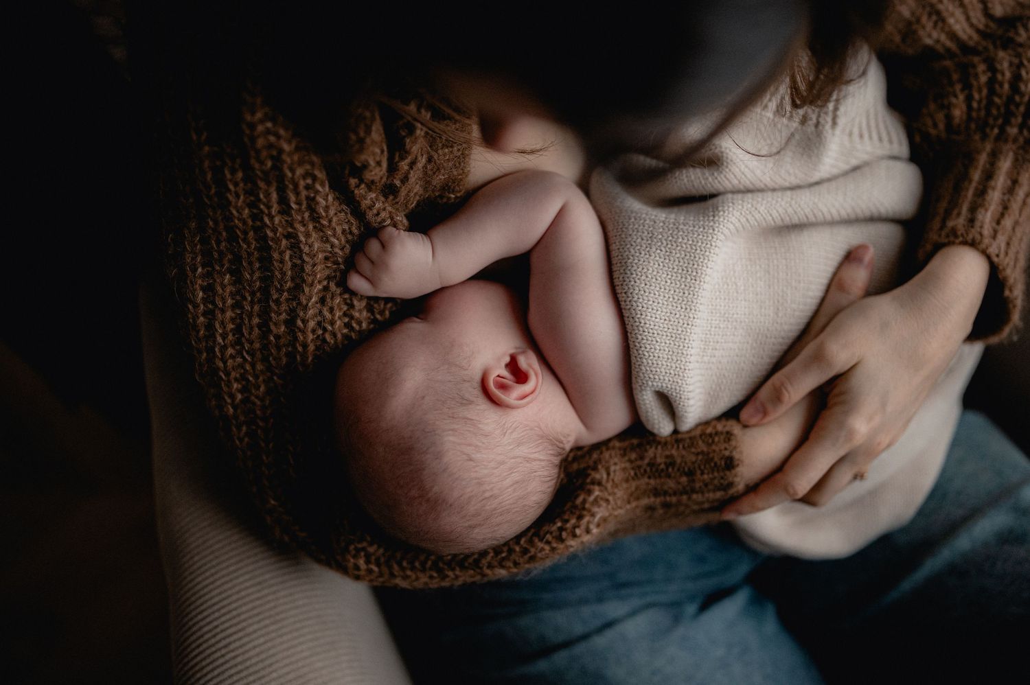 Close-up of newborn baby breastfeeding wrapped in warm knit blanket.