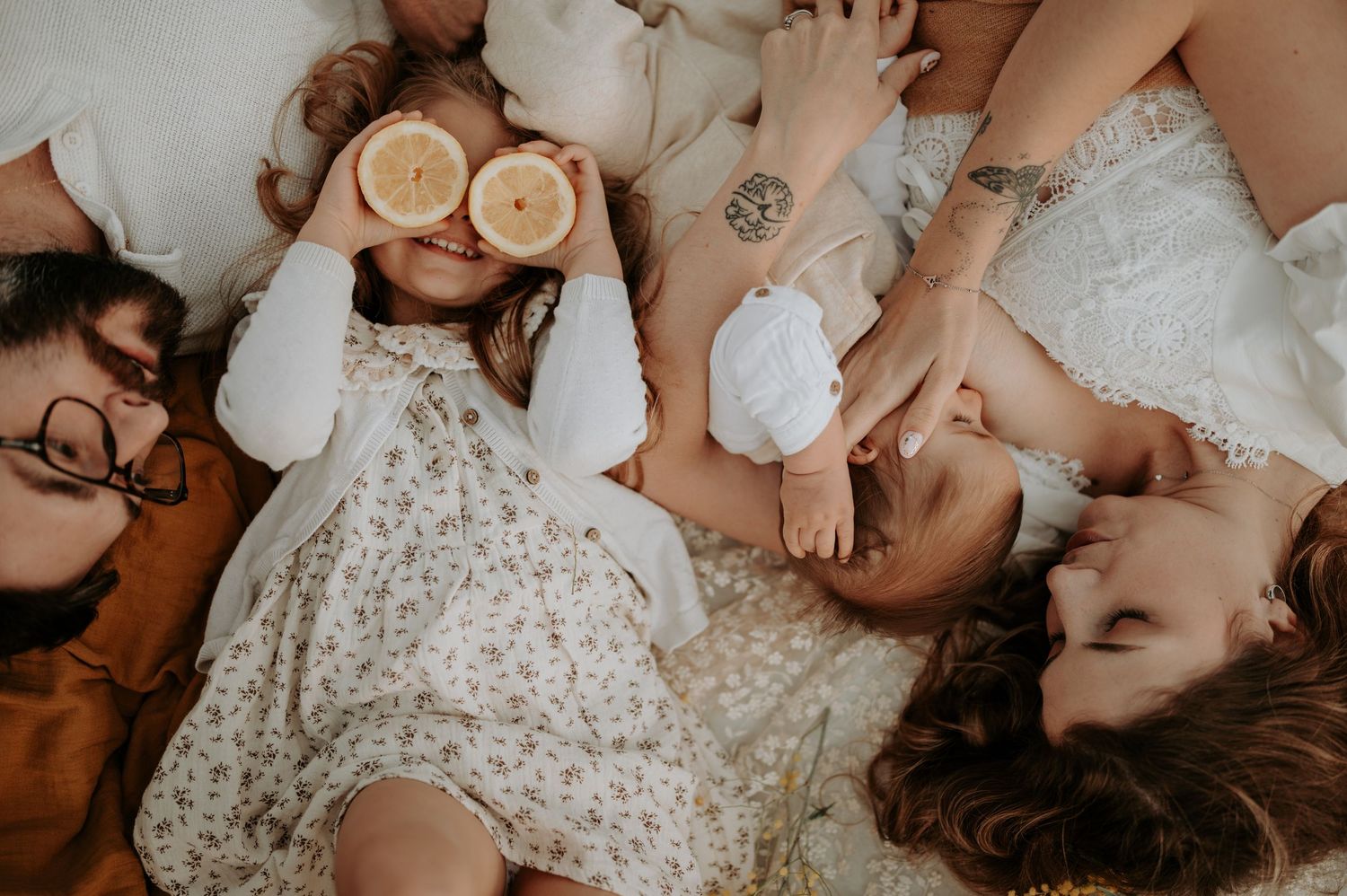 Family lying together on bed with children holding lemon halves in cozy indoor lifestyle photo.