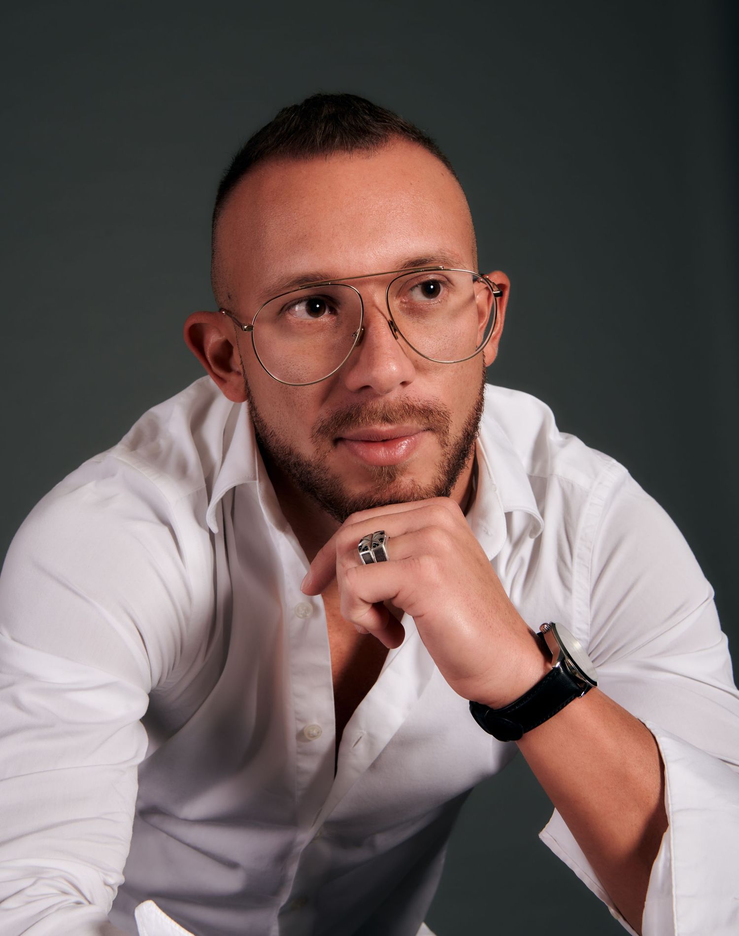 Man with glasses and white shirt in a thoughtful pose against gray background.