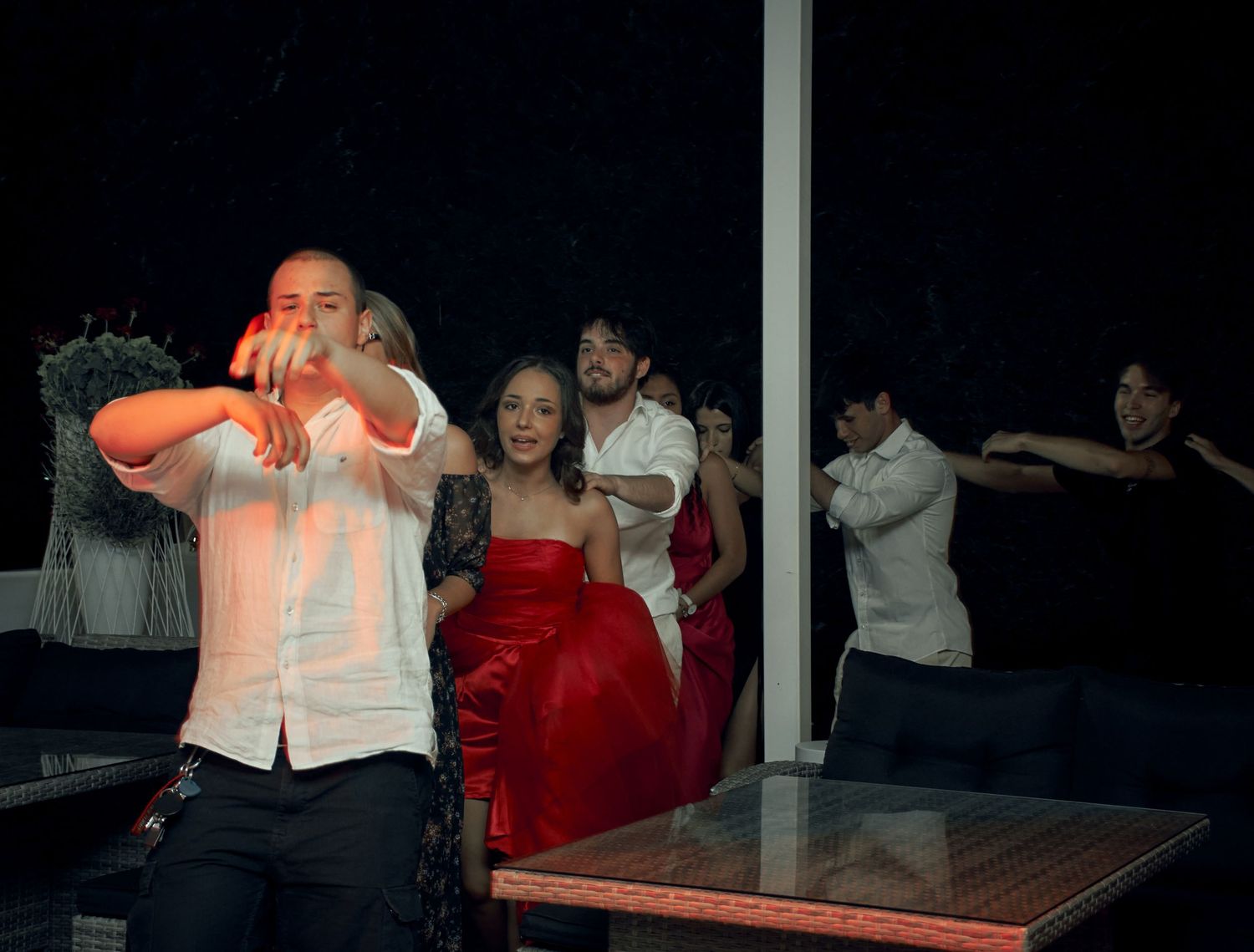 Group of elegantly dressed young people dancing and posing at an outdoor evening party.