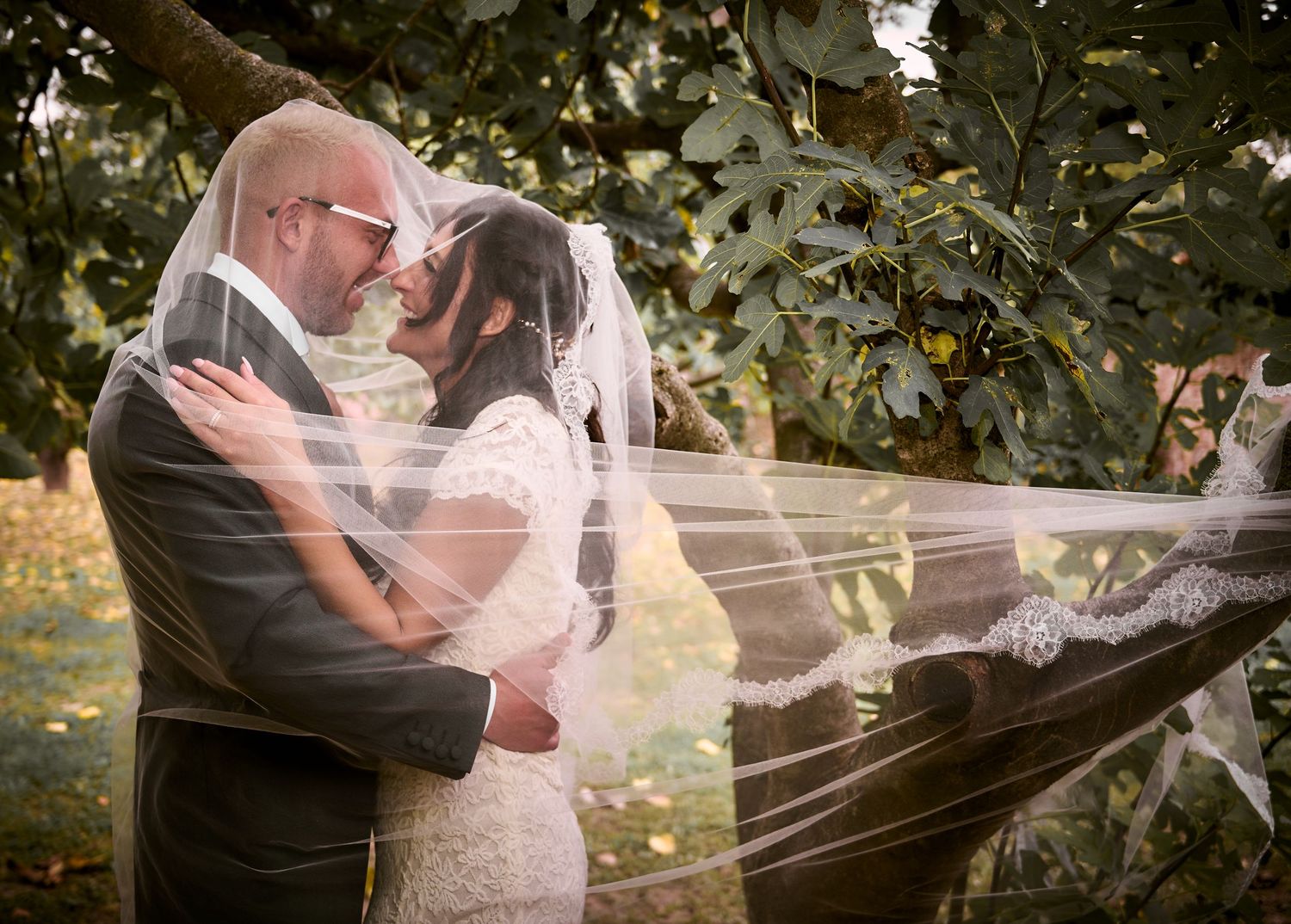 Bride and groom share a romantic moment under a veil outdoors at their wedding ceremony.