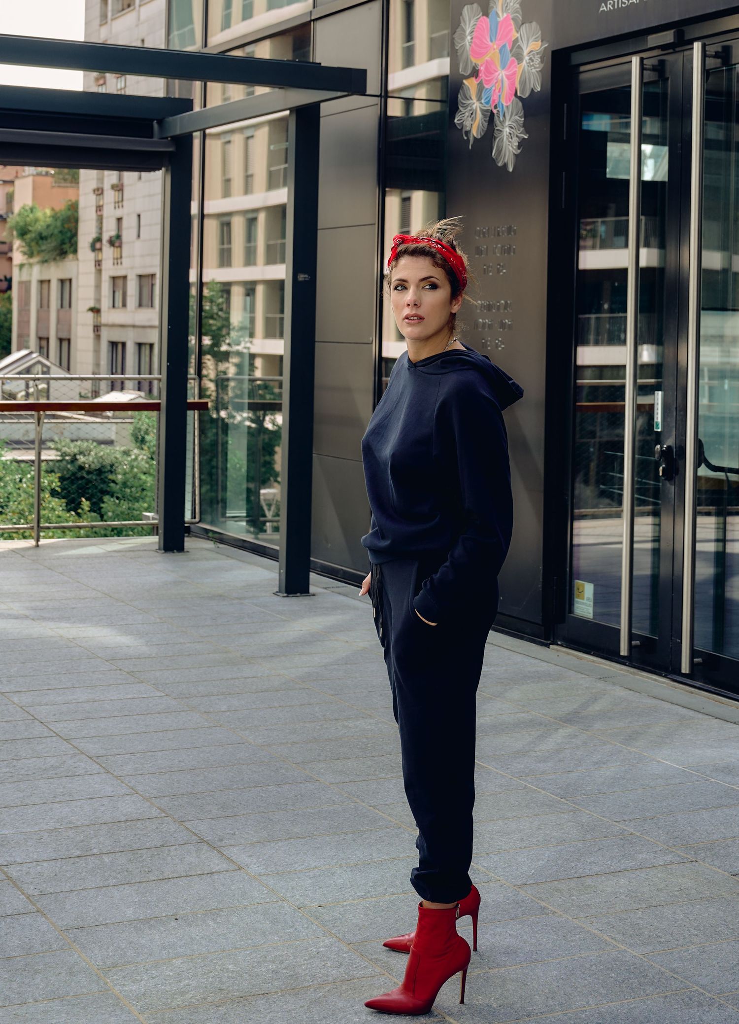 Woman in navy blue hoodie and red headband standing outside modern building with red ankle boots.