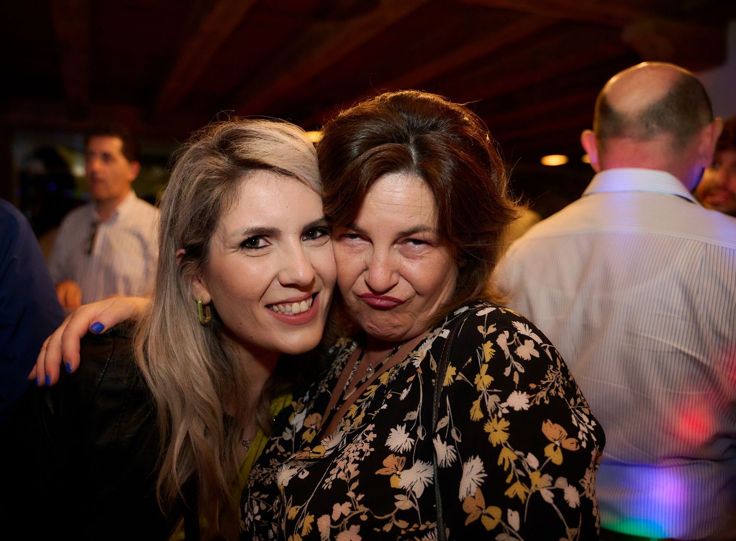Two women smiling and embracing affectionately at a lively evening party.