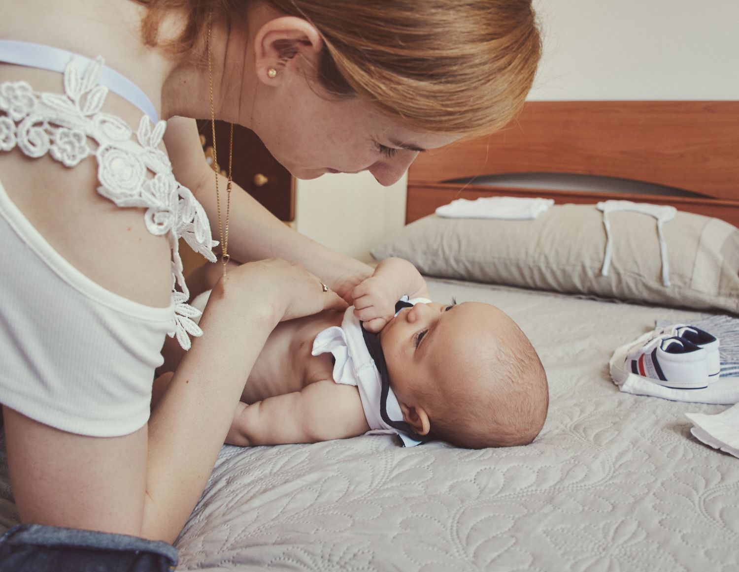 Young redhead mother tenderly interacting with her newborn baby lying on a bed during an intimate moment.