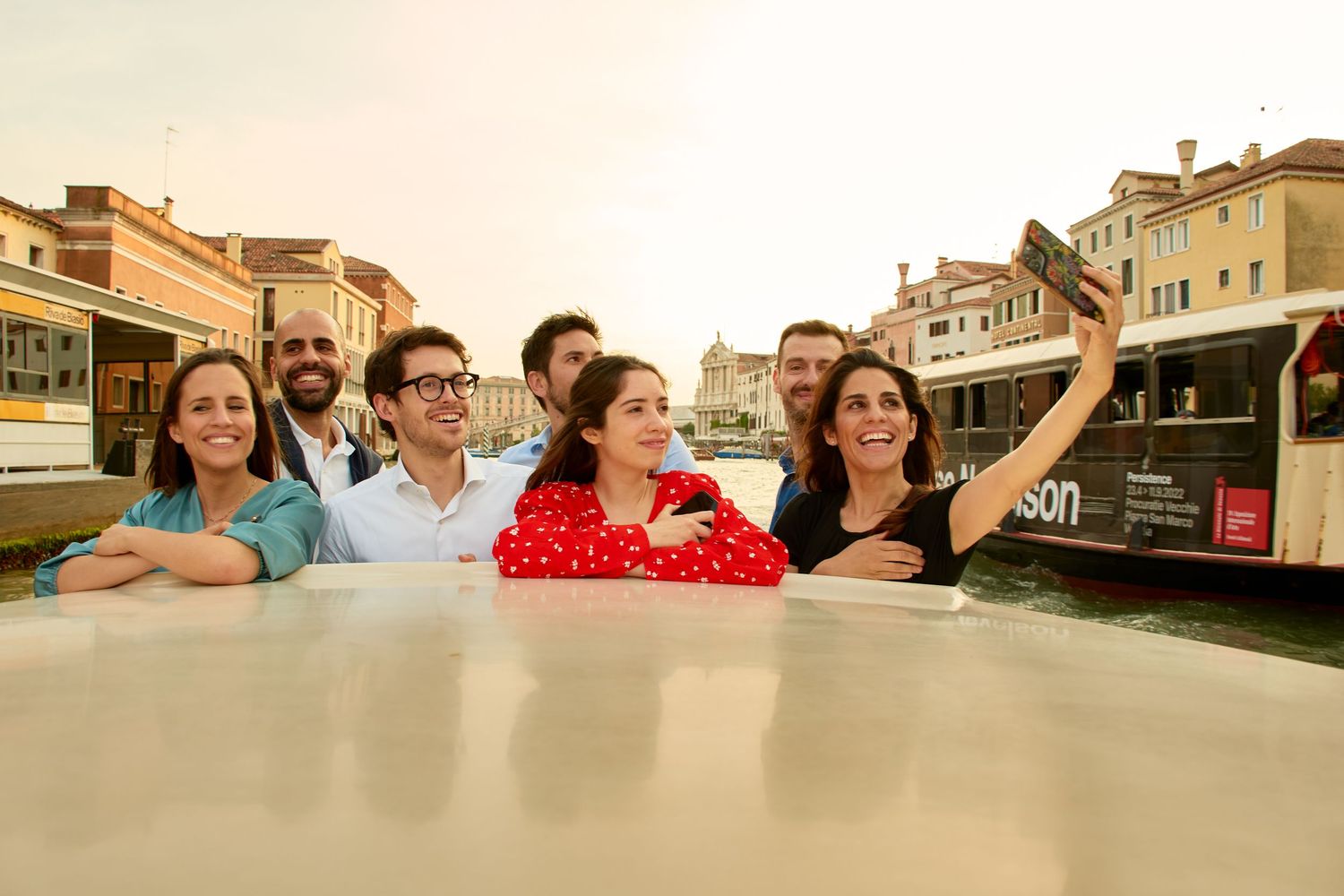 Group of friends taking a selfie on a boat along a Venice canal at sunset.