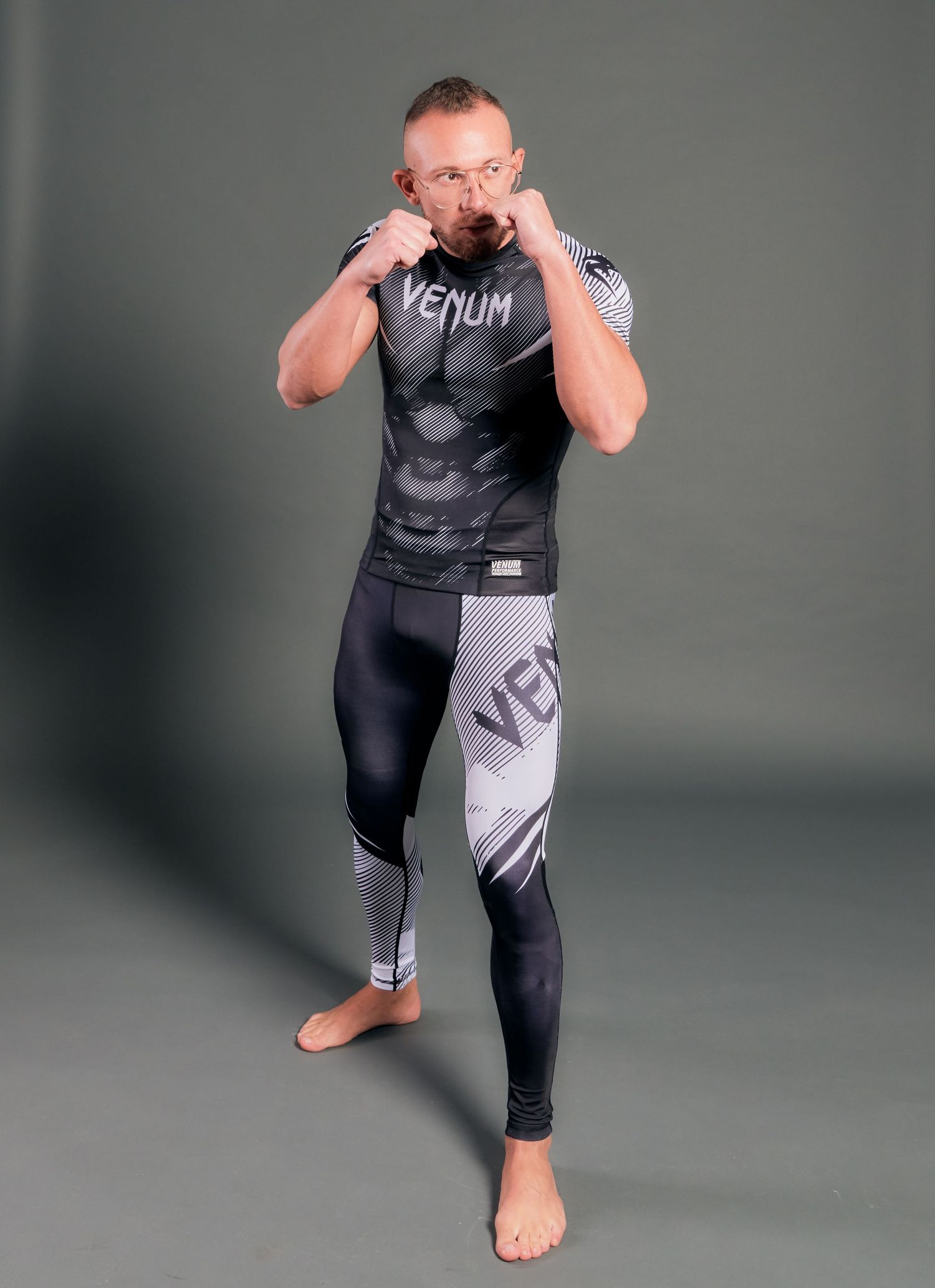 Male MMA fighter in Venum rashguard and compression tights in fighting stance on gray background.