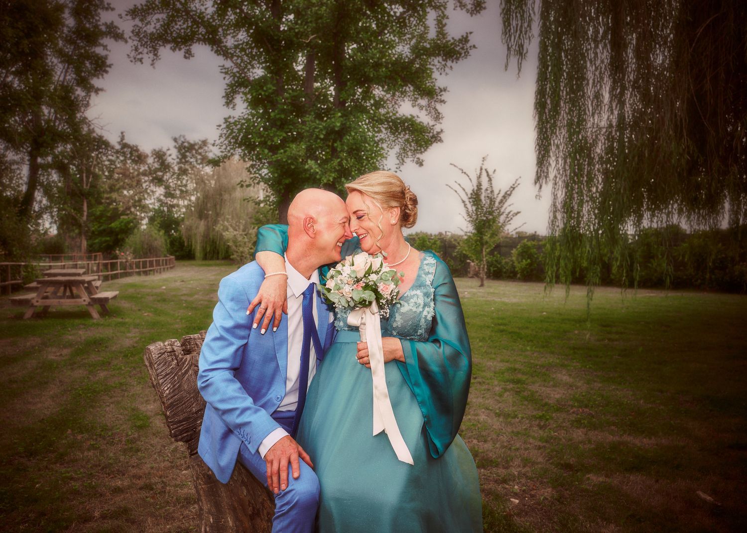 Bride and groom share romantic moment outdoors in teal wedding attire.