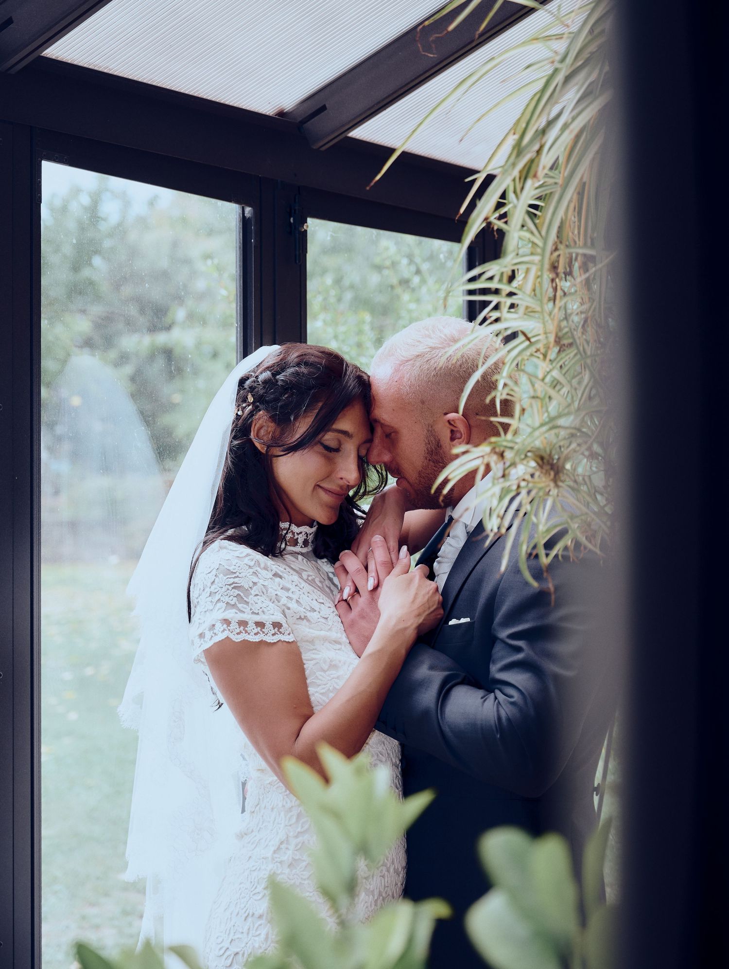 Bride and groom share intimate moment in greenhouse wedding portrait.