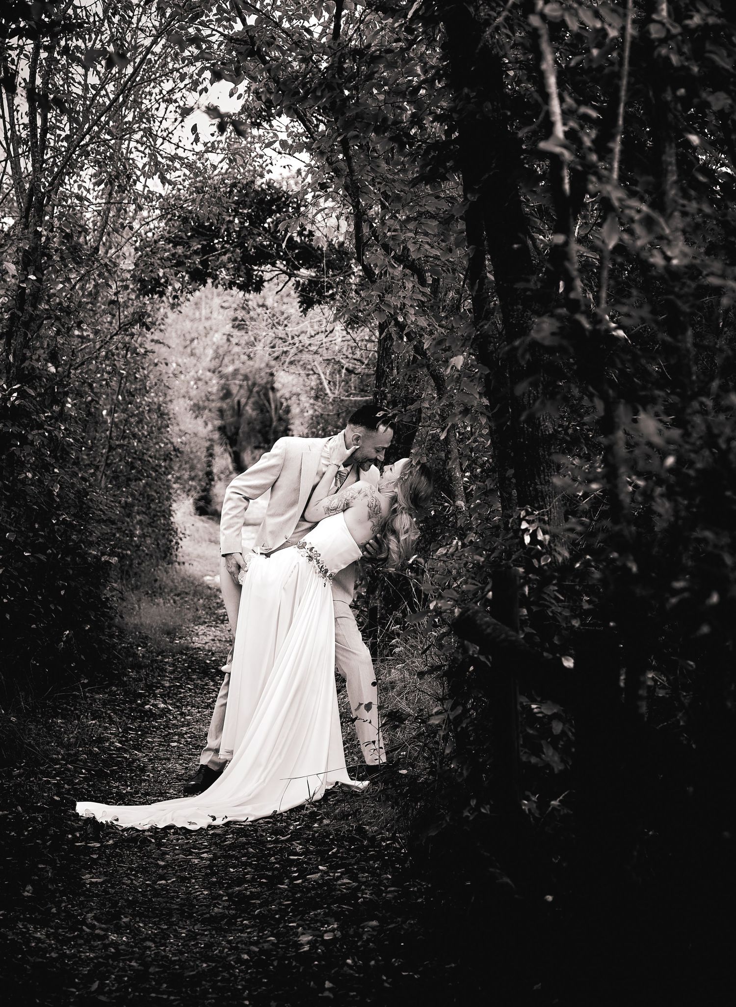 Romantic black and white photo of couple kissing in forest path.