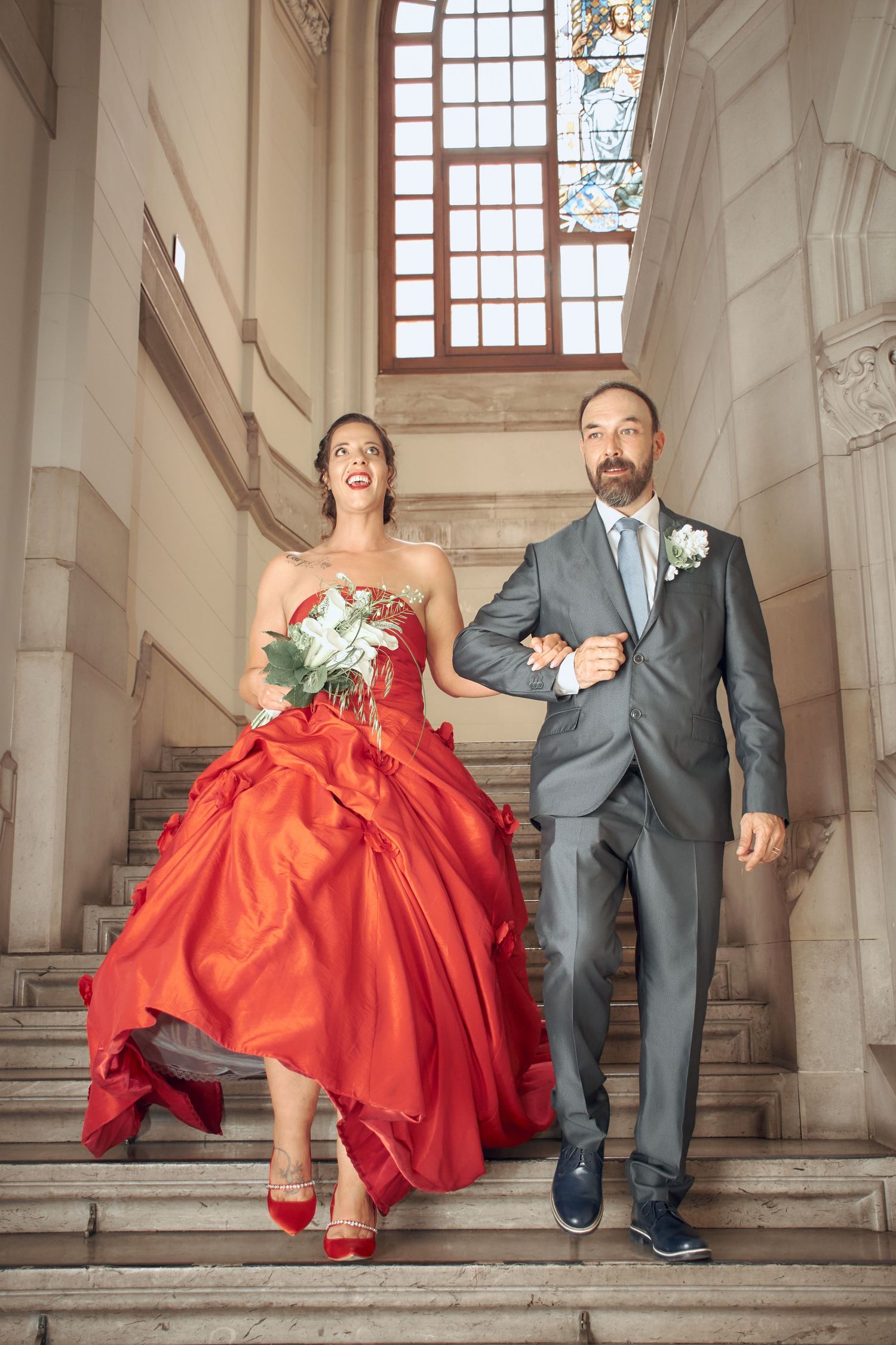Couple descends grand staircase, bride in stunning red ball gown.