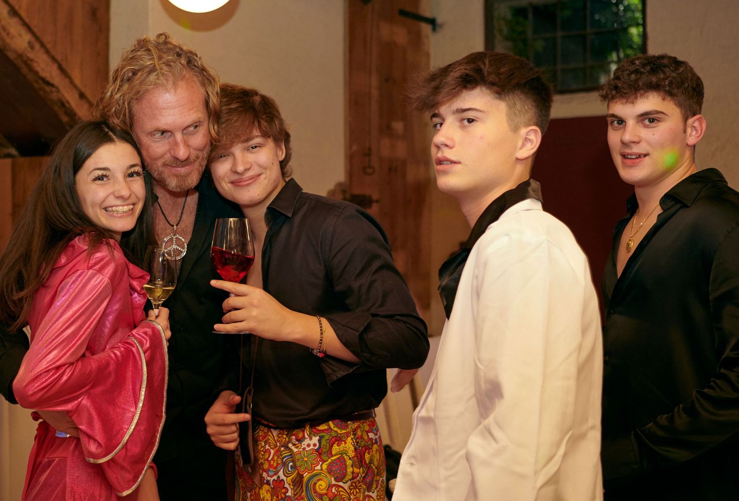 A group of five people in colorful outfits pose together at a festive indoor gathering.