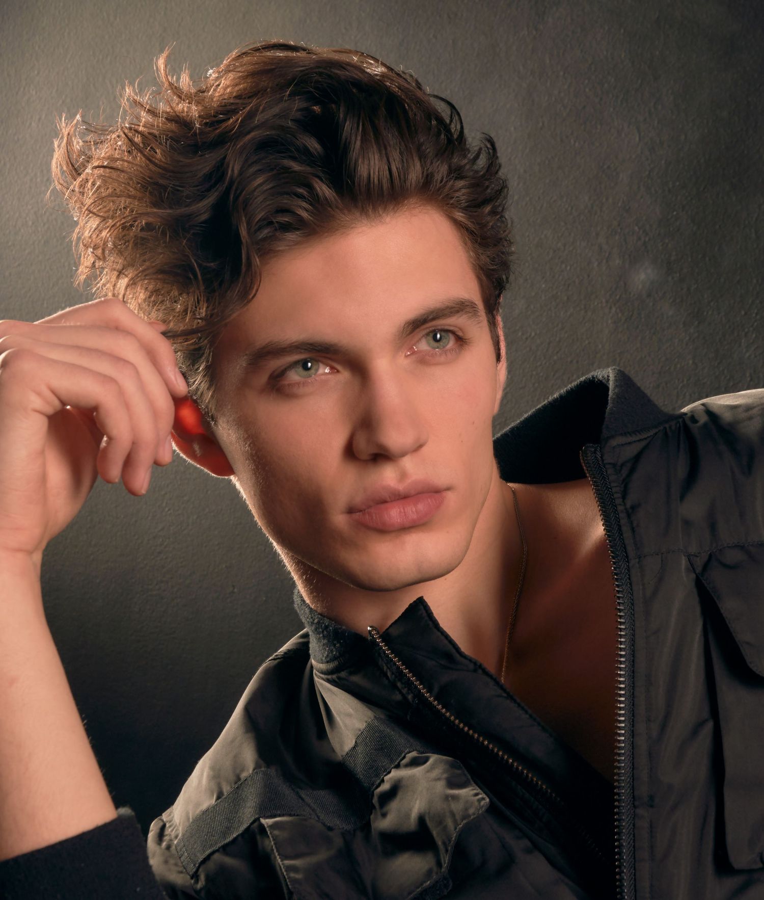 Young man with curly brown hair and green eyes posing in a dark jacket.