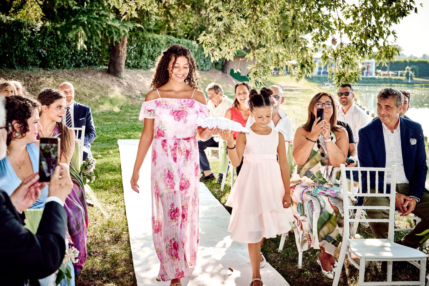 Woman in floral dress walks young girl down the aisle at an outdoor wedding.