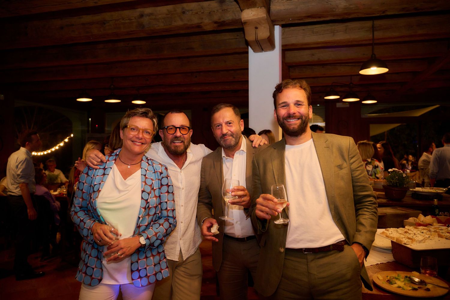 Four men smiling and holding champagne glasses at an indoor social event.