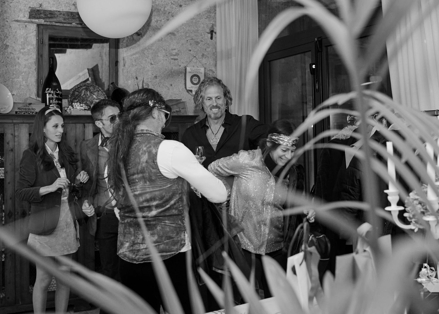 A black and white photo of guests mingling and exchanging gifts at an indoor social event.