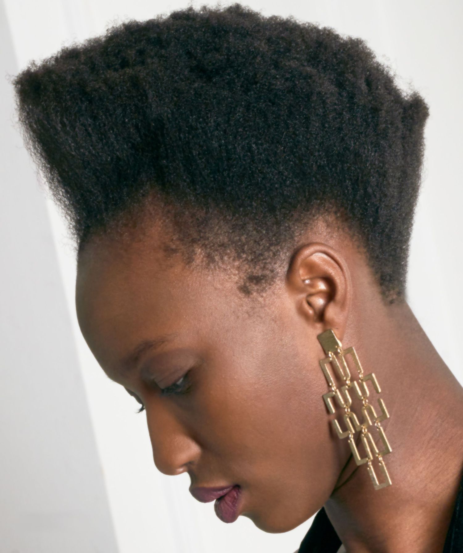 Close-up profile portrait of Black woman with natural tapered haircut wearing gold geometric earrings.
