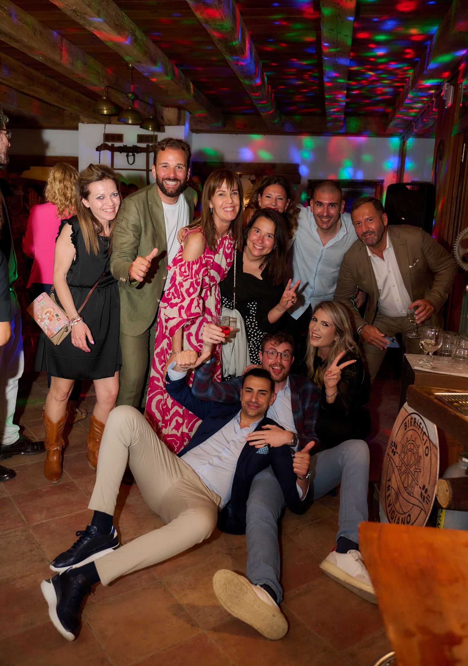 Large group of friends posing playfully under colorful disco lights at a party.